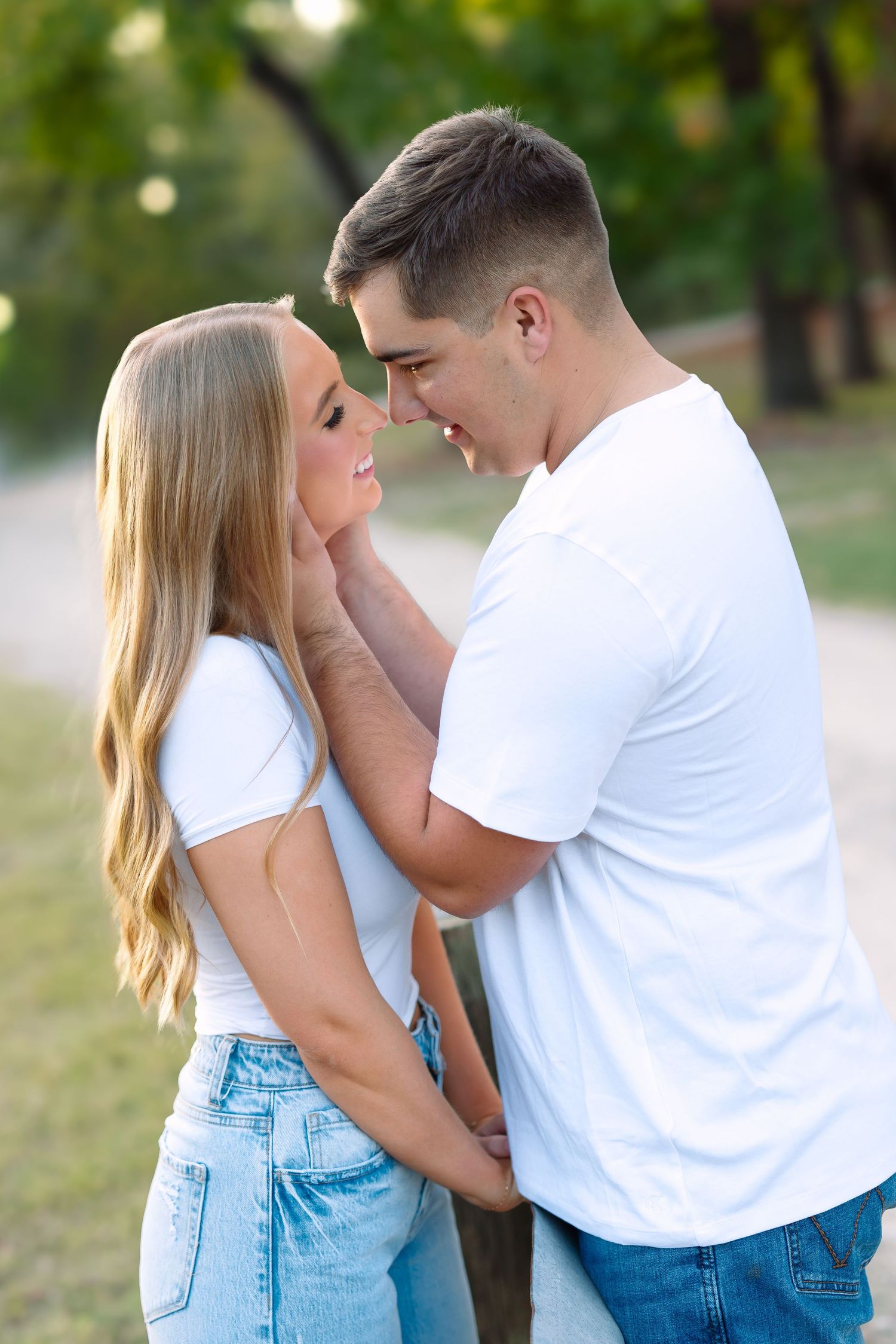 Young couple in matching white tees and jeans sharing a romantic moment outdoors in a green park setting.