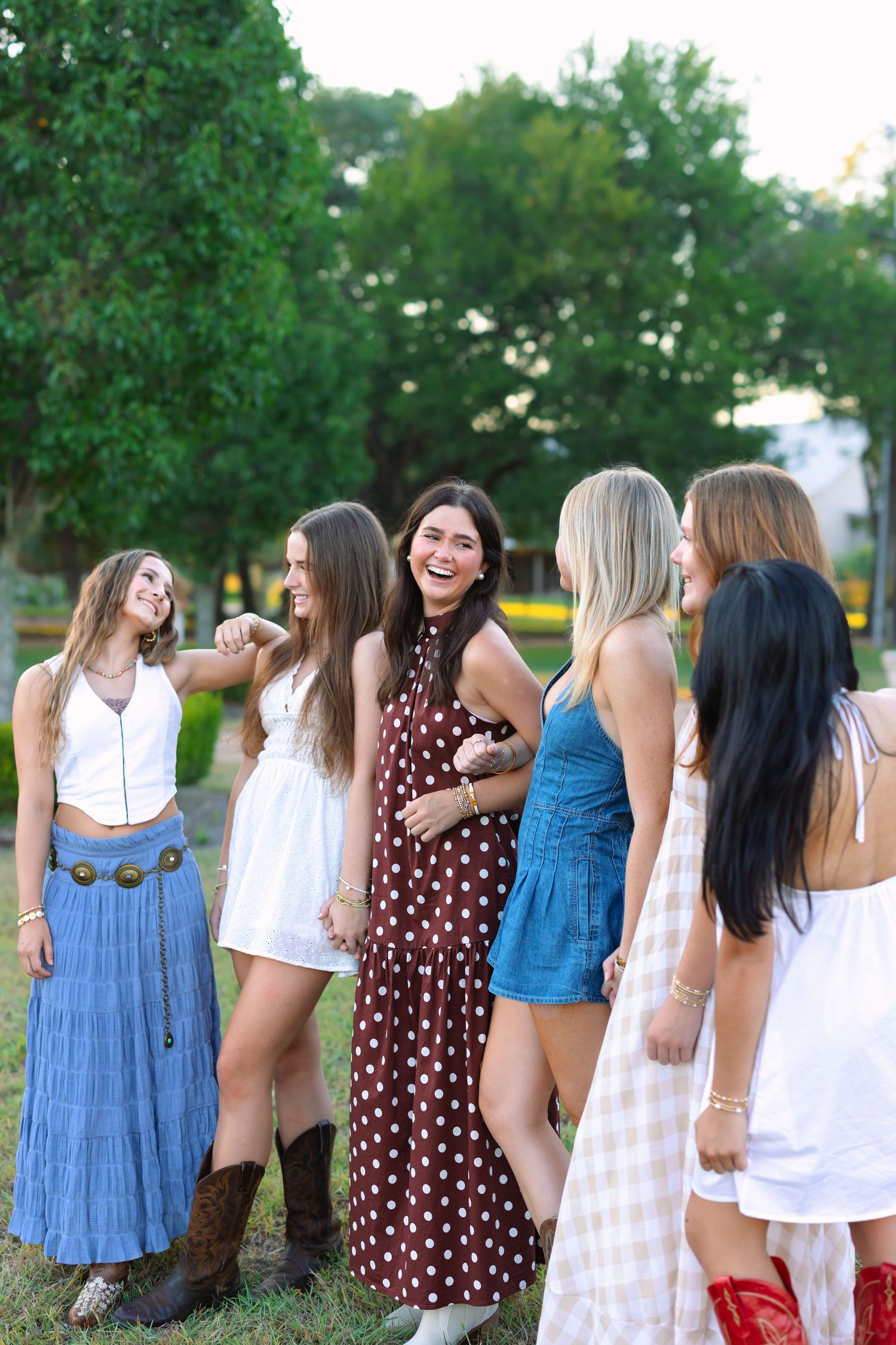 Friends in summer dresses share a candid moment of laughter outside a rustic barn.