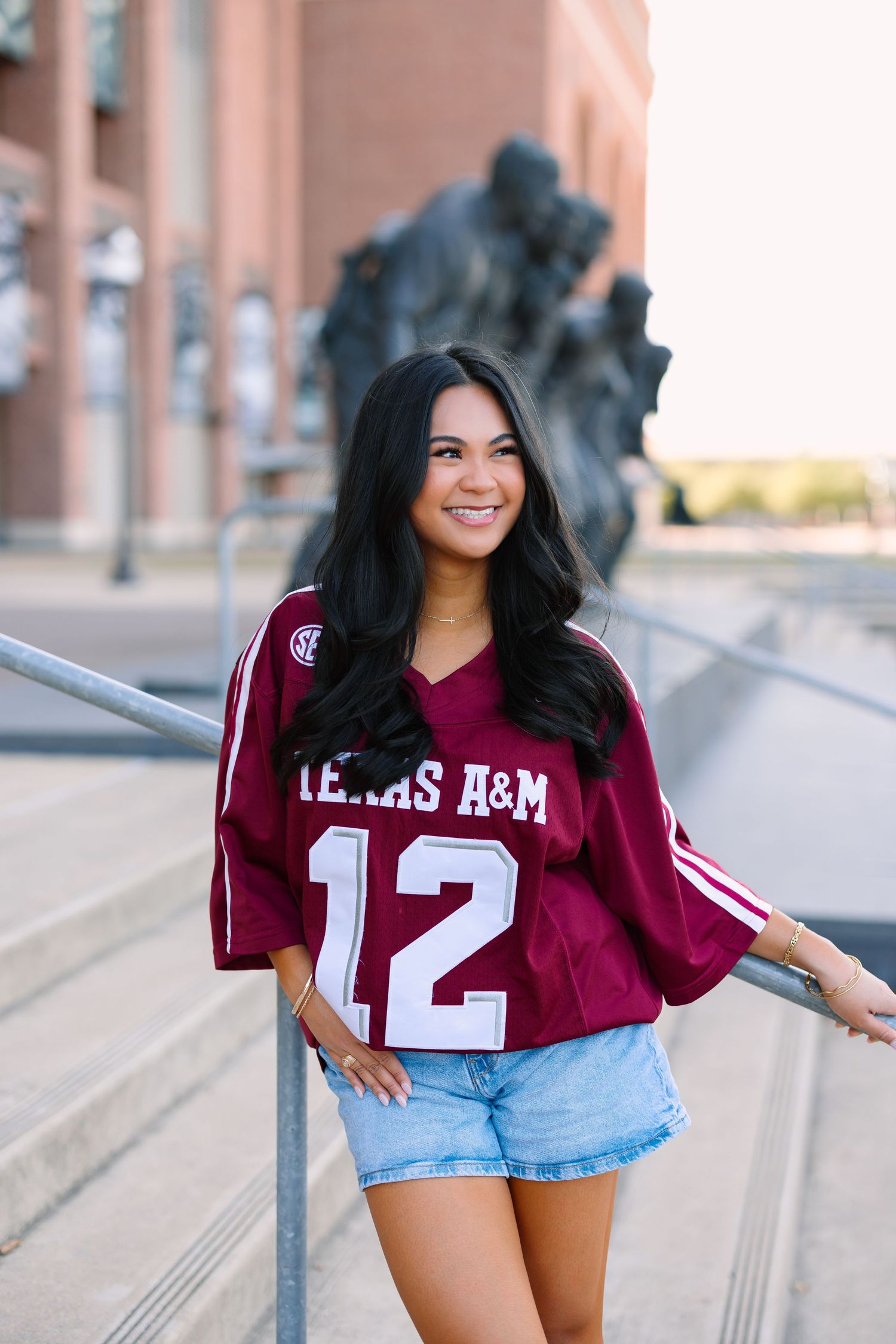 College student wearing a Texas A&M maroon jersey and denim shorts poses outdoors on campus steps.