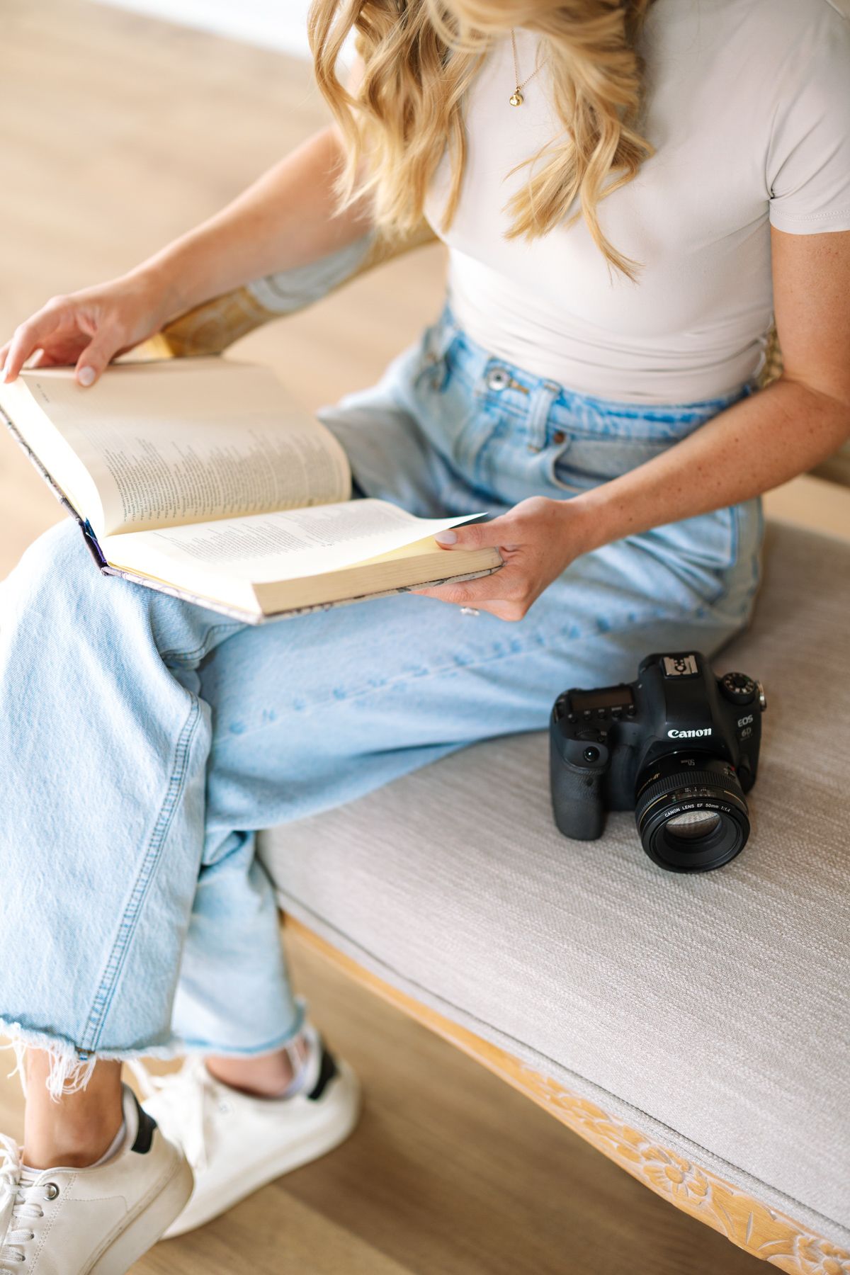 Person relaxing on rattan bench with camera and book in casual attire.