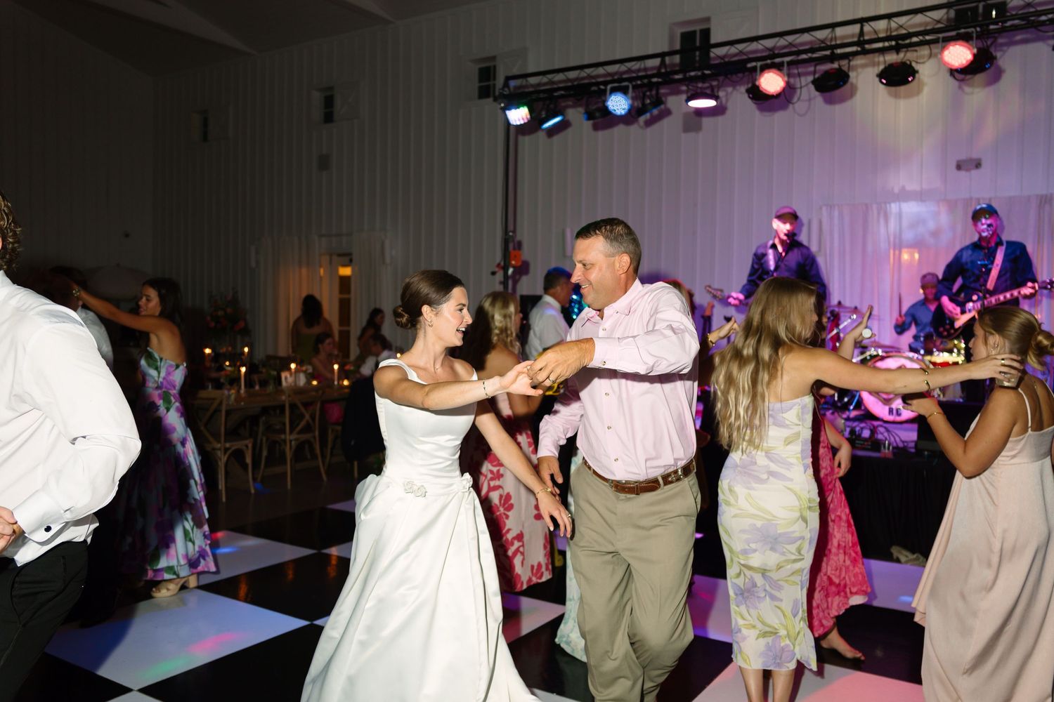 Bride and groom dancing with guests on checkered dance floor at wedding reception with live band performing.
