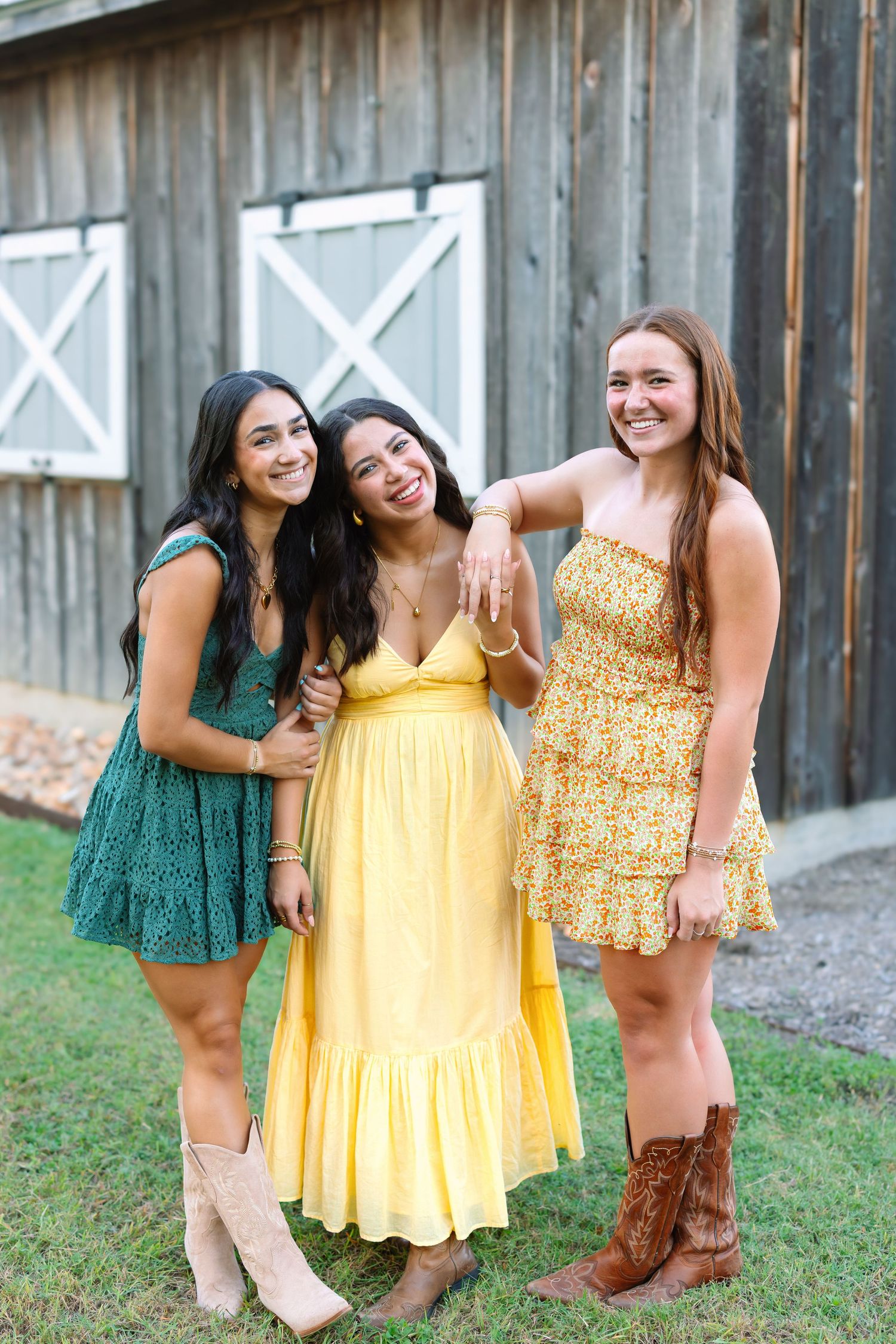 Group of women in yellow and green sundresses posing by rustic barn wall.