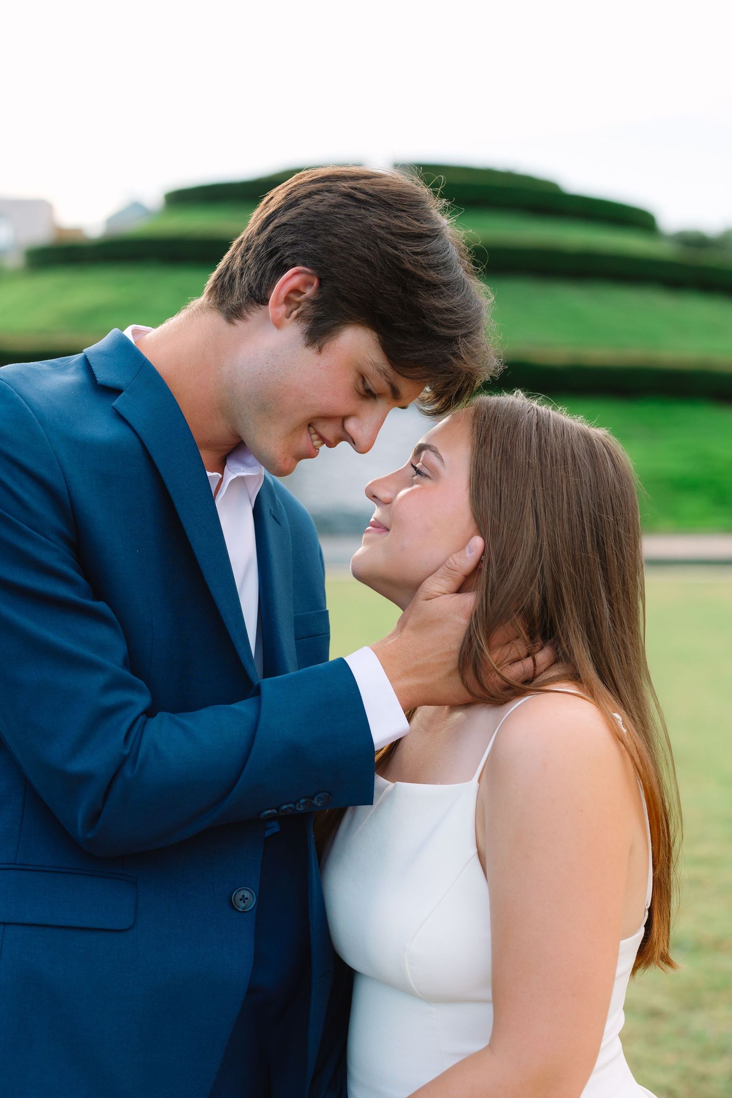 Romantic couple in blue suit and white dress share intimate moment outdoors.