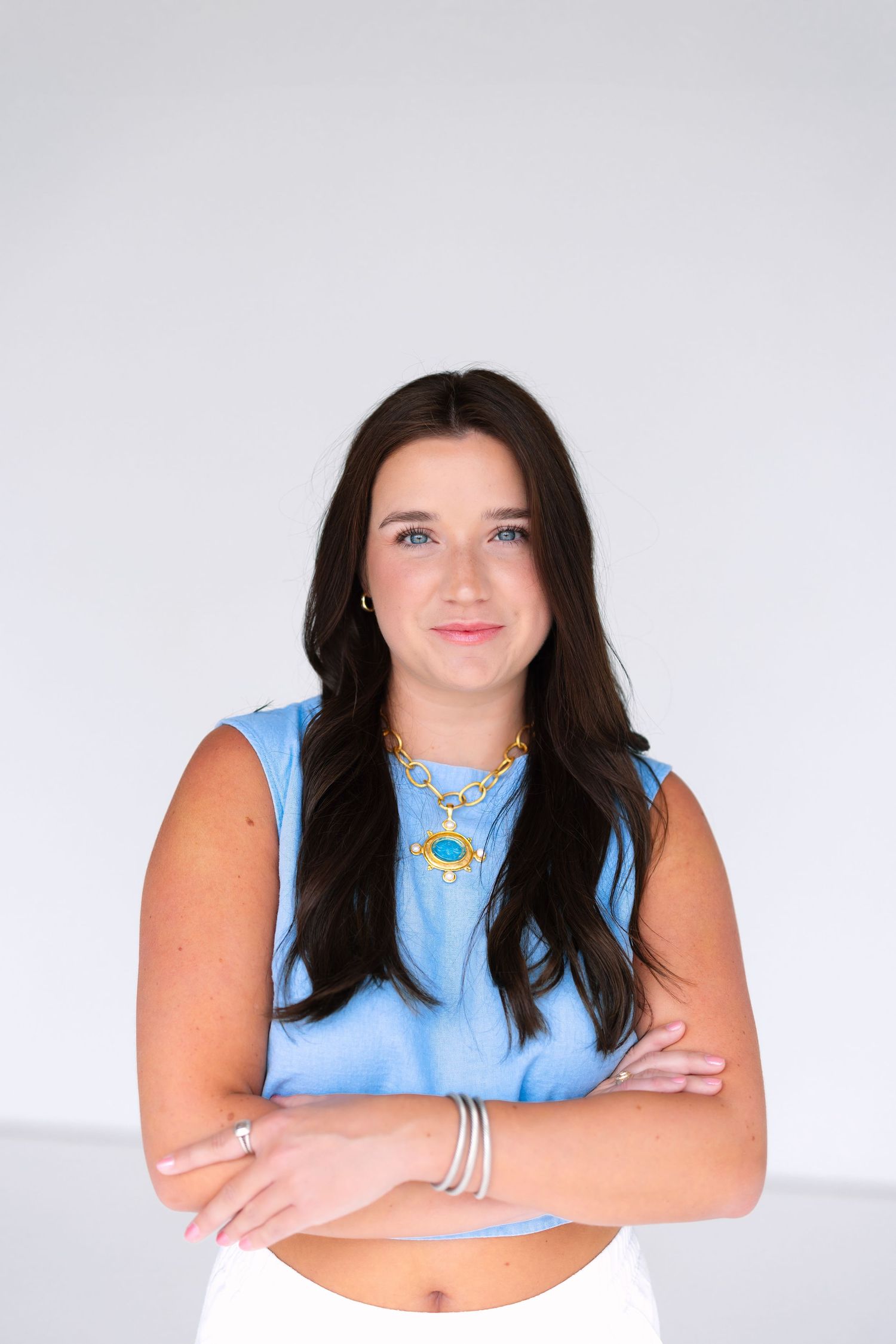 Portrait against white background wearing light blue sleeveless top and jewelry.