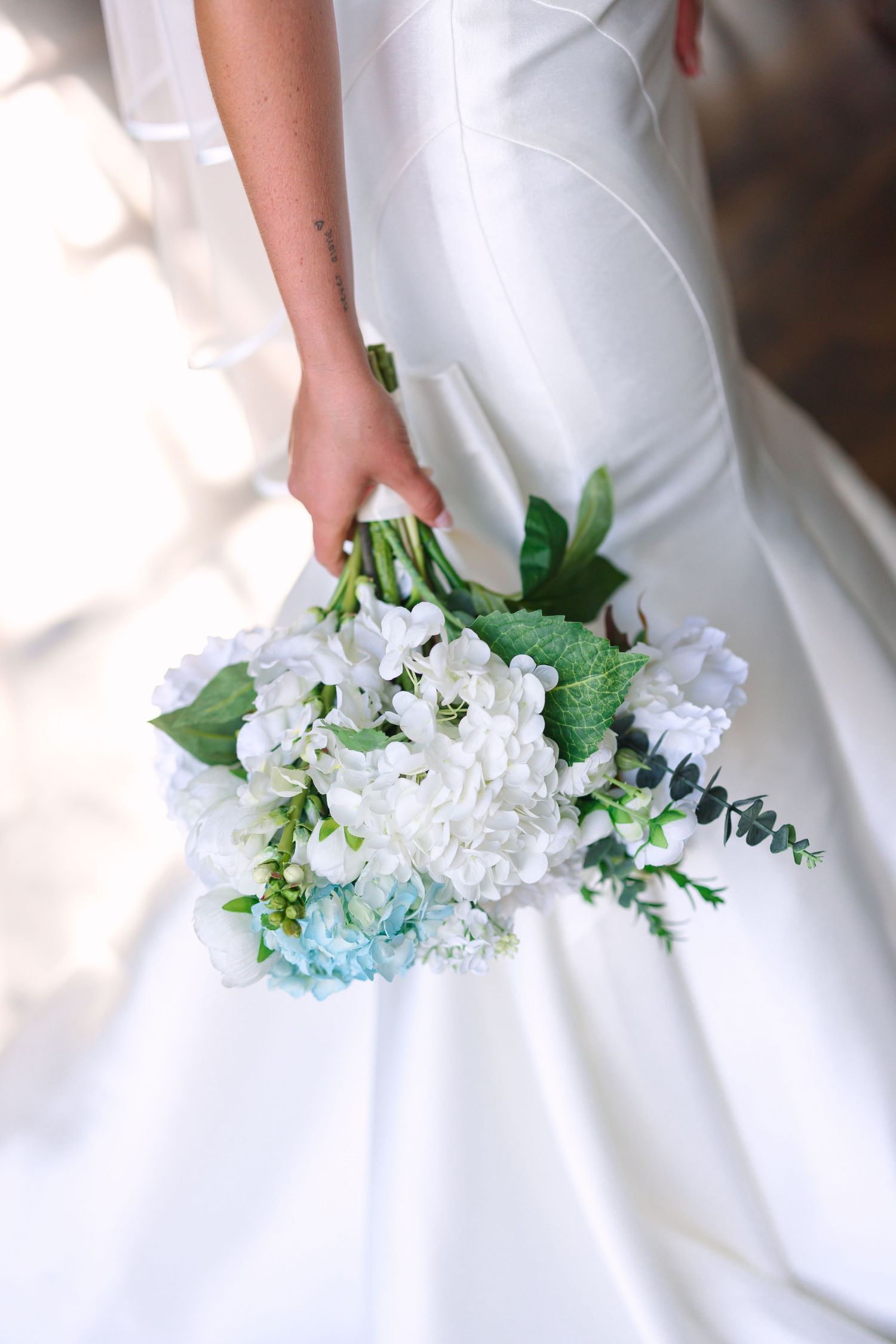 White and blue hydrangea bouquet detail against wedding dress.