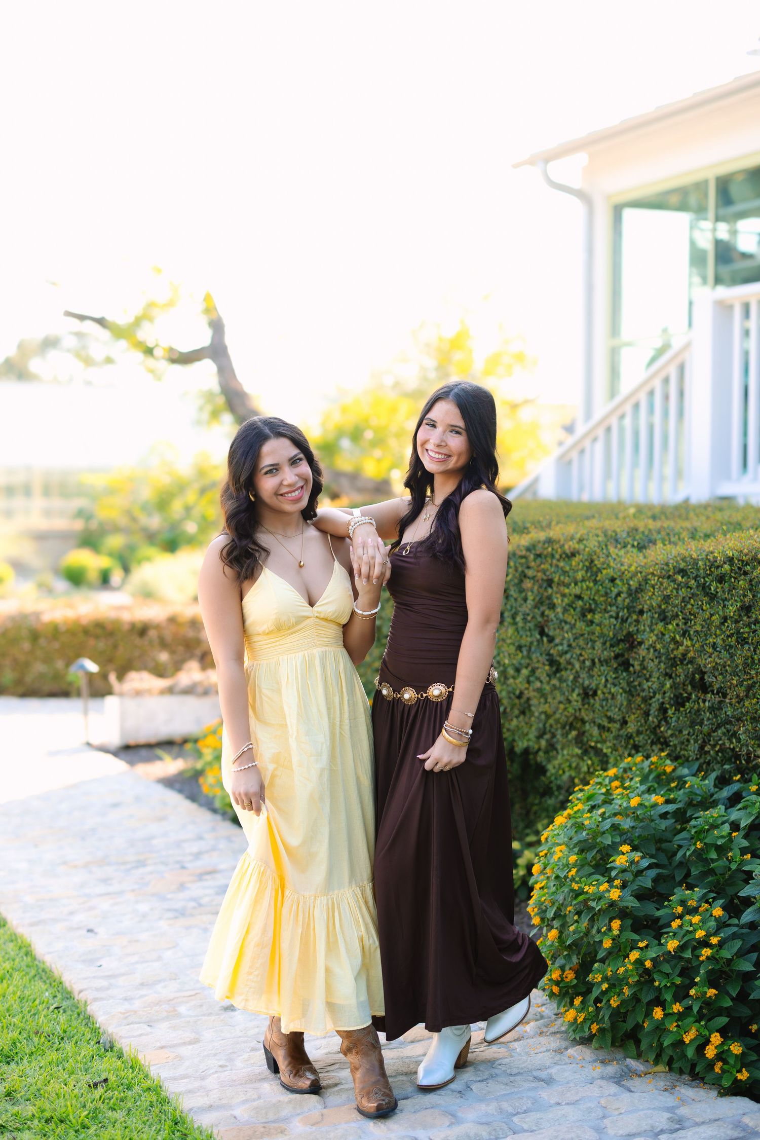 Two friends in contrasting dresses pose together by blooming yellow flowers.