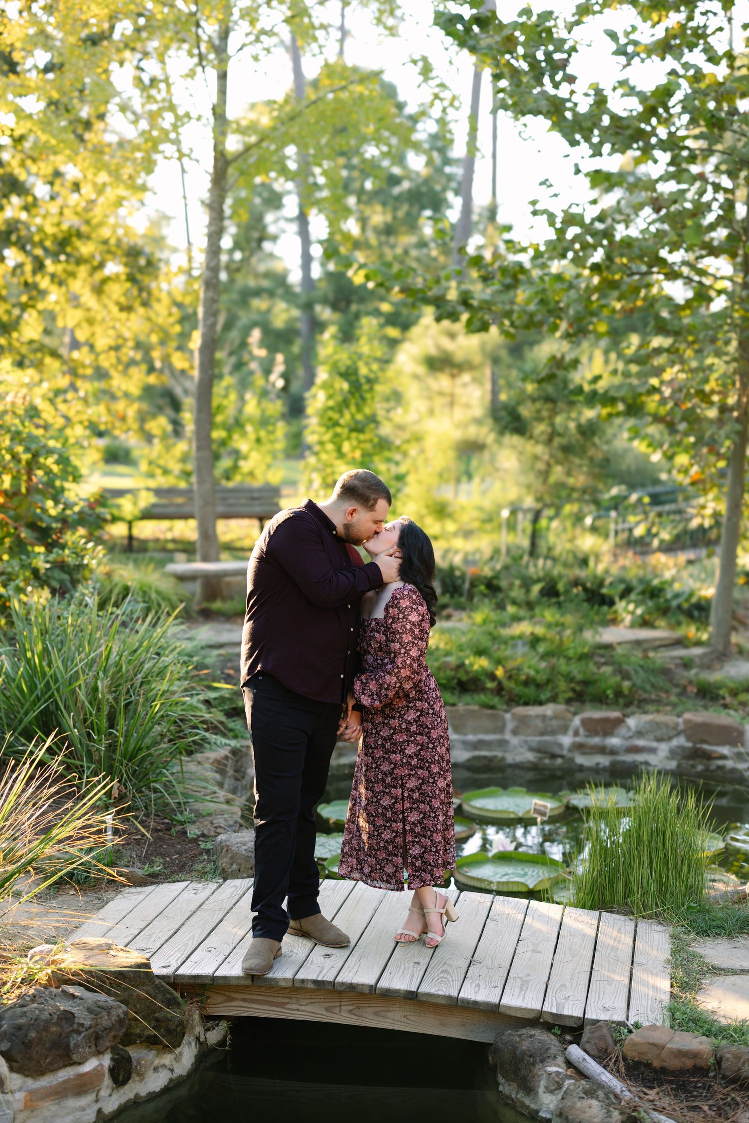 Couple sharing intimate moments on a wooden bridge surrounded by lush greenery.