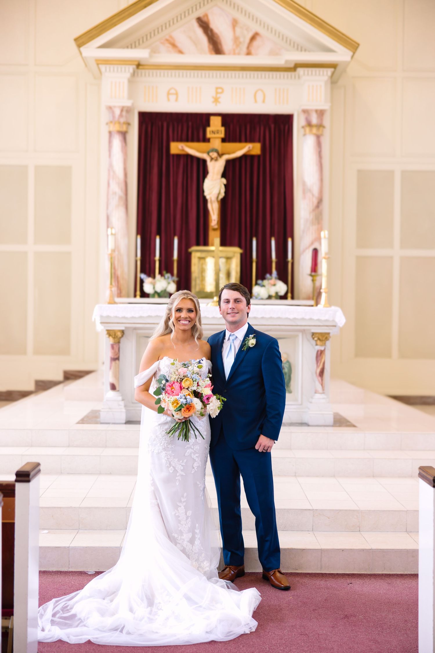Bride and groom pose together at church altar with crucifix backdrop on their wedding day.