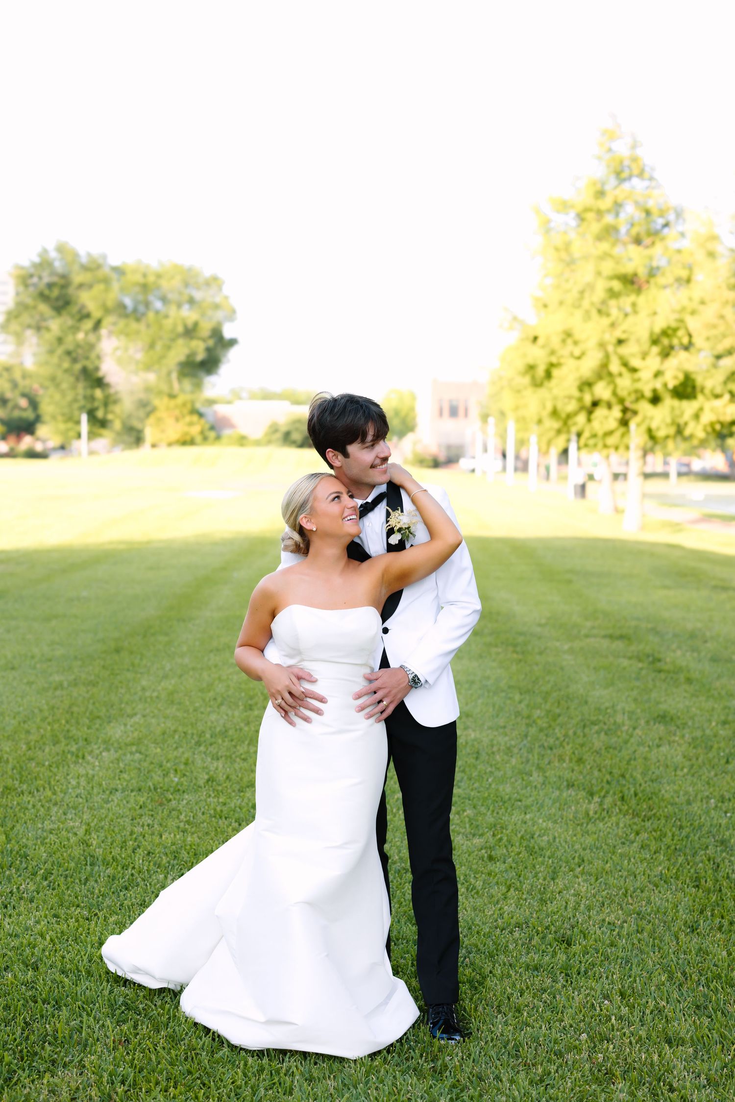 Bride and groom embrace lovingly on a lush green lawn during their outdoor wedding portrait session.