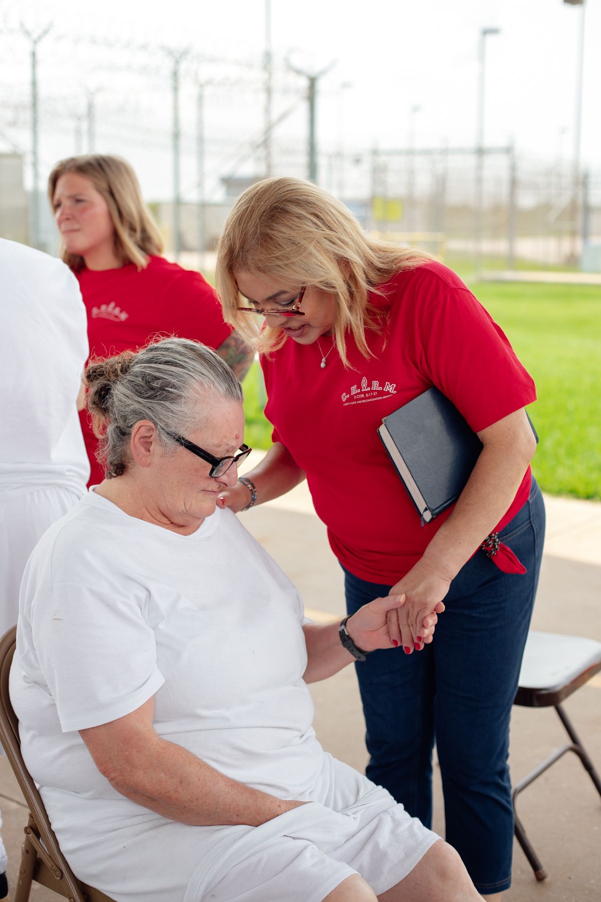 Prison ministry volunteers in red shirts interacting with inmates in white clothing.