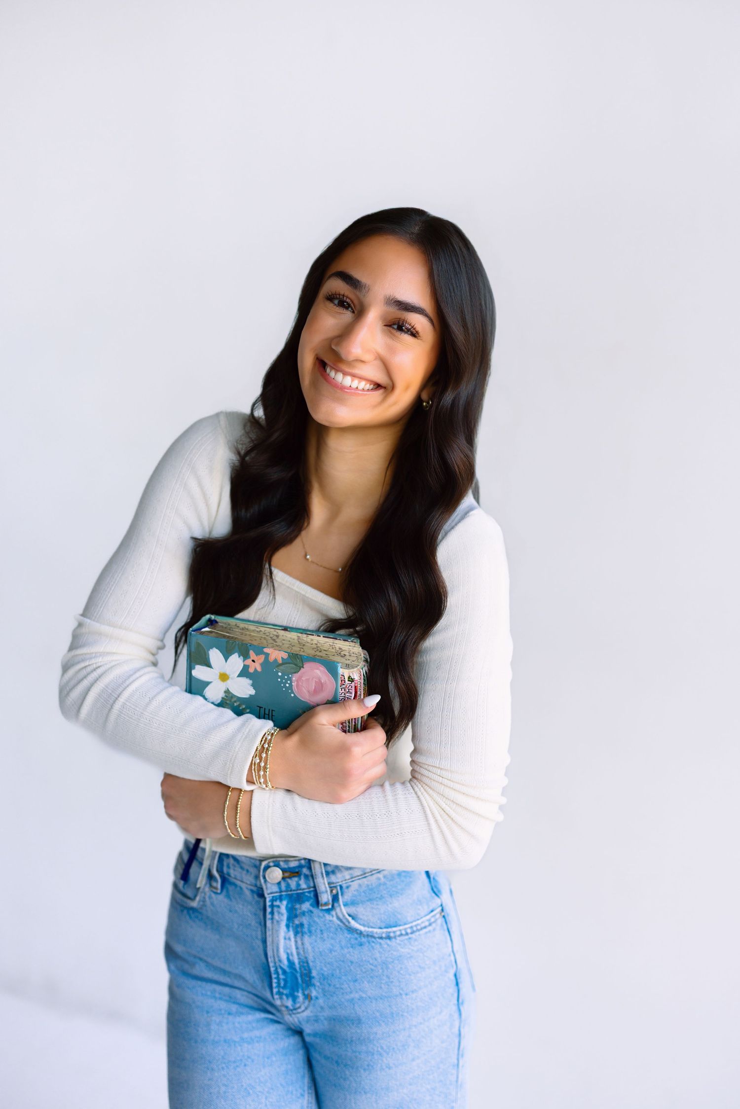 Casual portrait holding floral mug wearing white long sleeve top and jeans against white background.