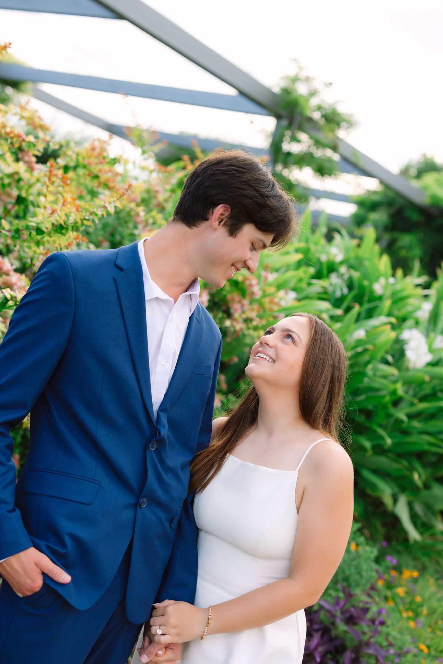Couple in blue suit and white top share loving moment in garden setting.