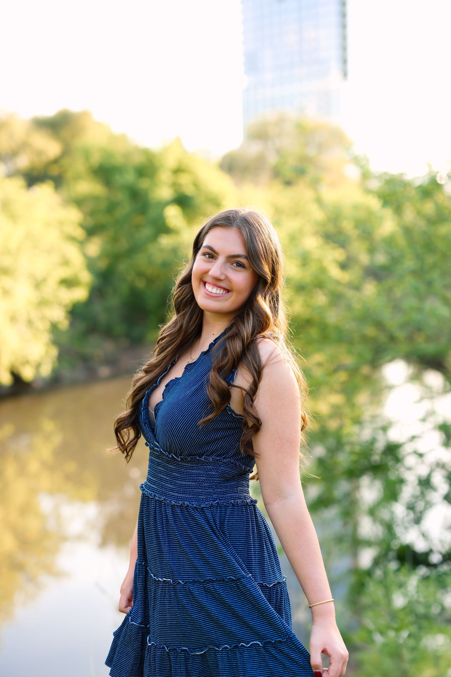 Person in navy blue dress poses by waterfront during golden hour.
