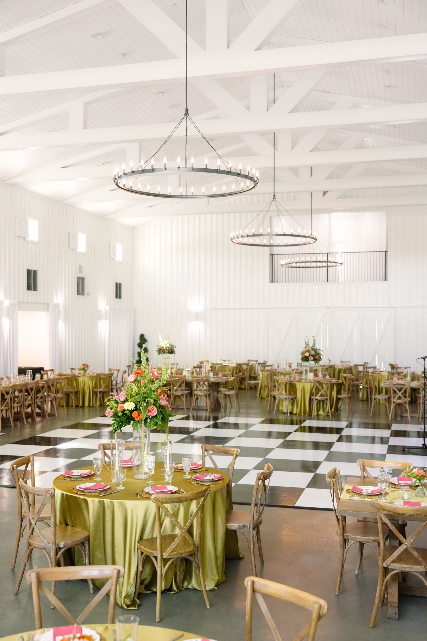 Elegant wedding reception hall with olive green tablecloths, floral centerpieces, wood chairs, and black-and-white checkered dance floor.