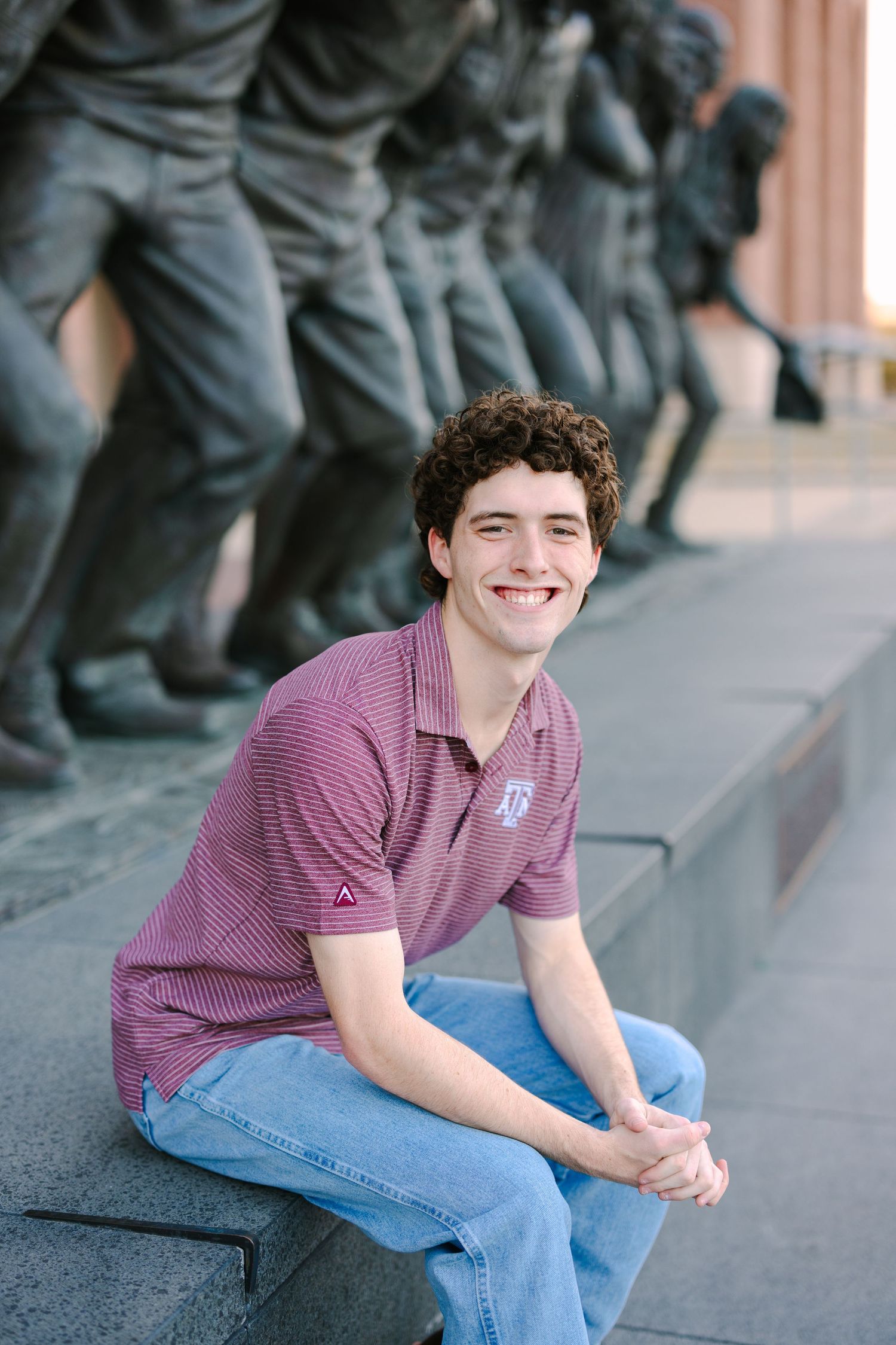 Student in purple polo and jeans sits casually by campus statue display.