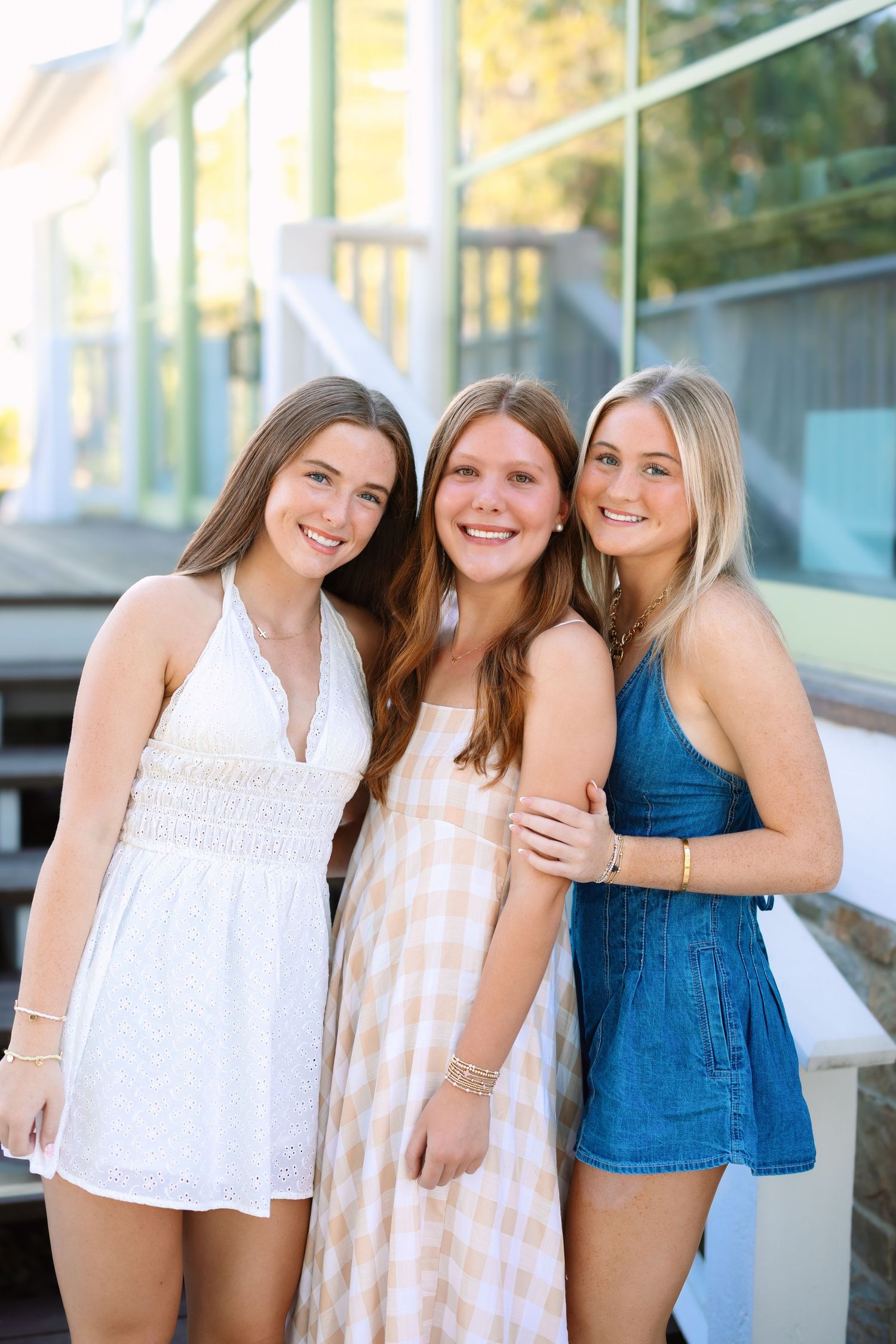 Friends in light summer tops pose together against a bright window background.