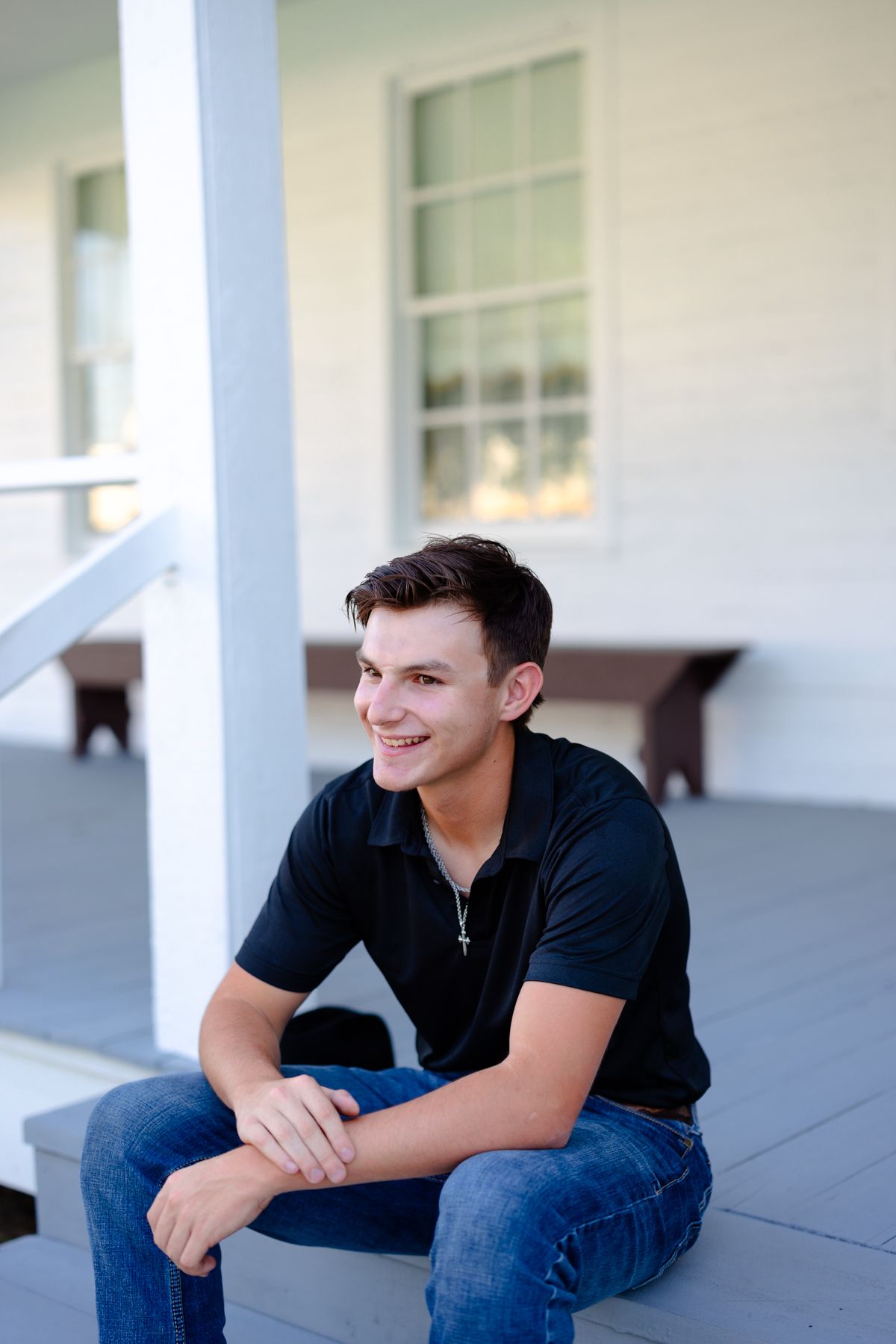 Person relaxing on white porch wearing casual black attire in natural lighting.
