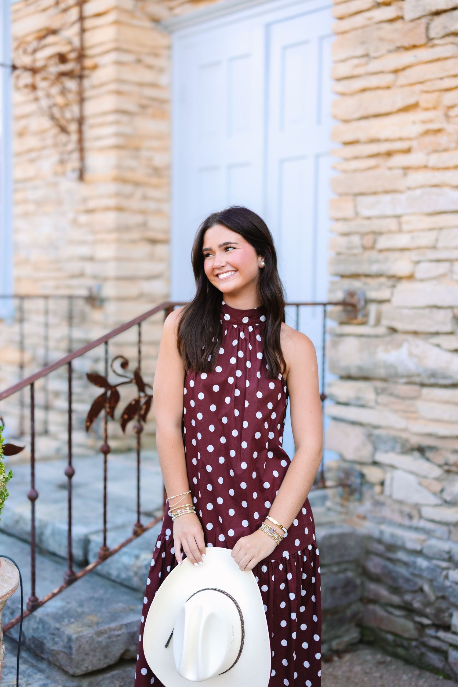 Portrait series featuring someone in a burgundy polka dot dress holding a white hat near stone steps.