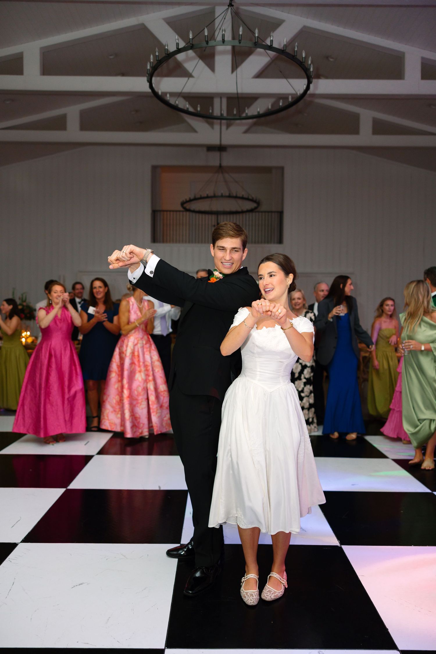A couple shares their first dance on a black and white checkered floor at a formal wedding reception.