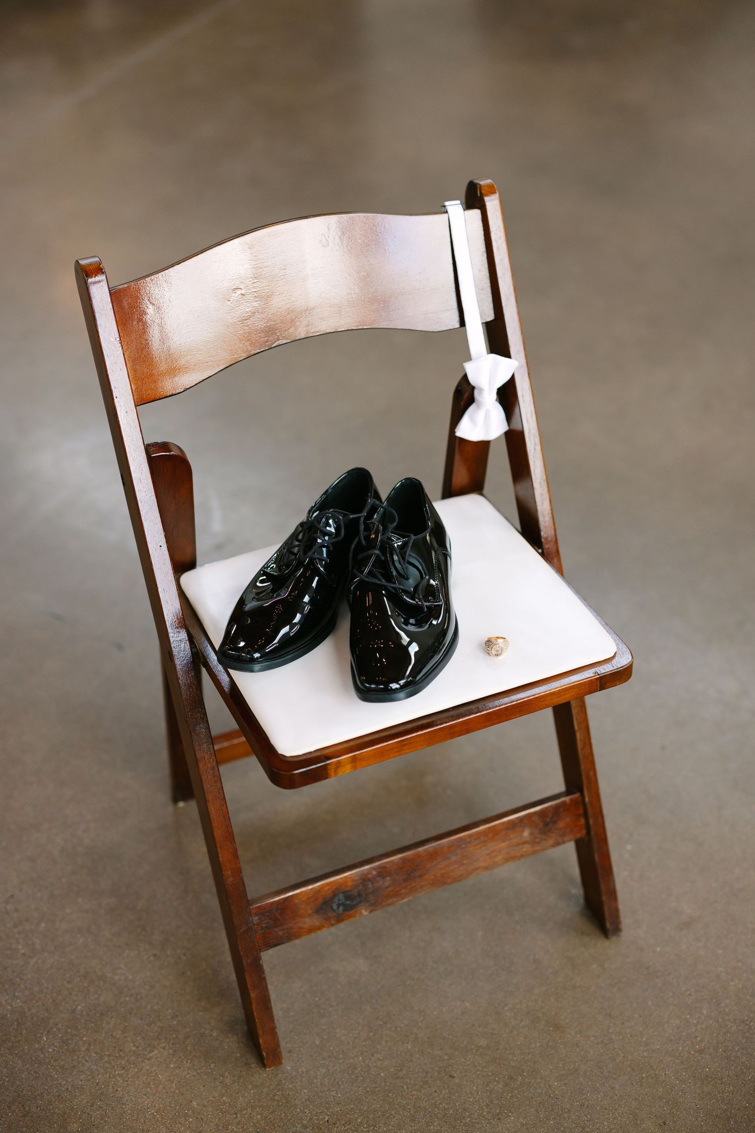 Black dress shoes placed on a wooden folding chair against dark background.