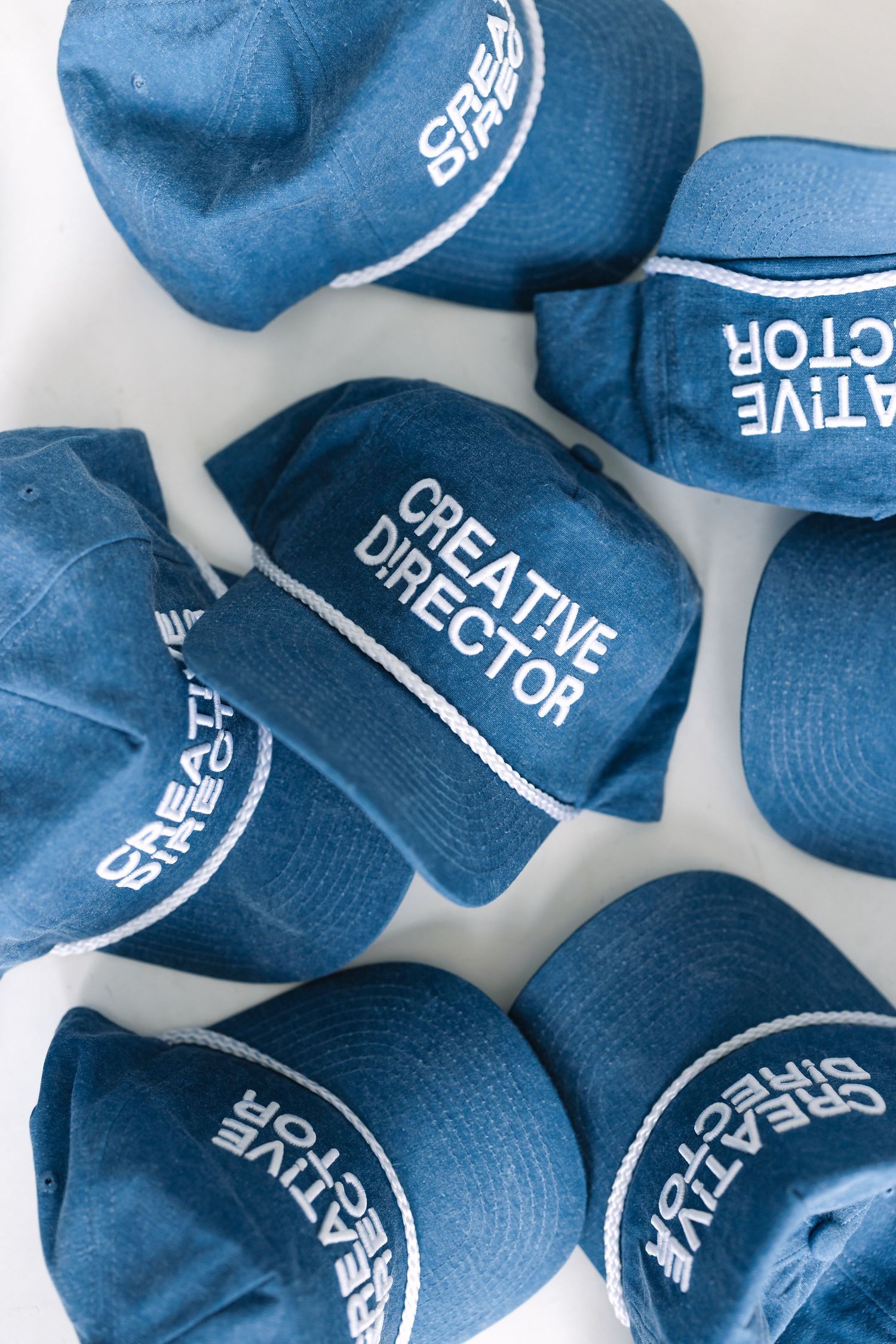 Collection of blue baseball caps with Creative Director text laid out on white surface.