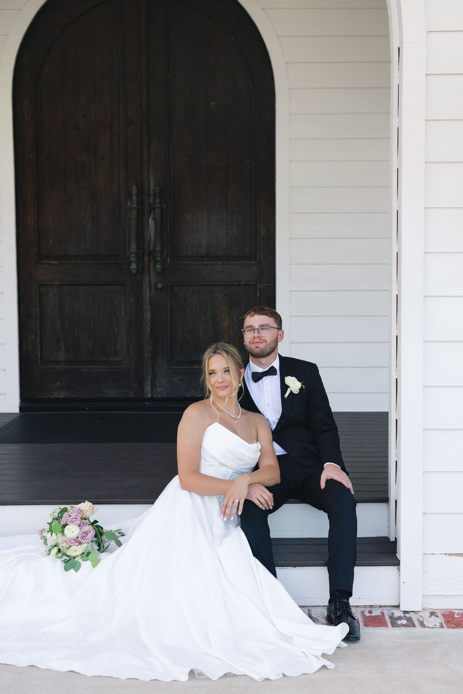 Newlyweds share an intimate moment while sitting on white porch steps.