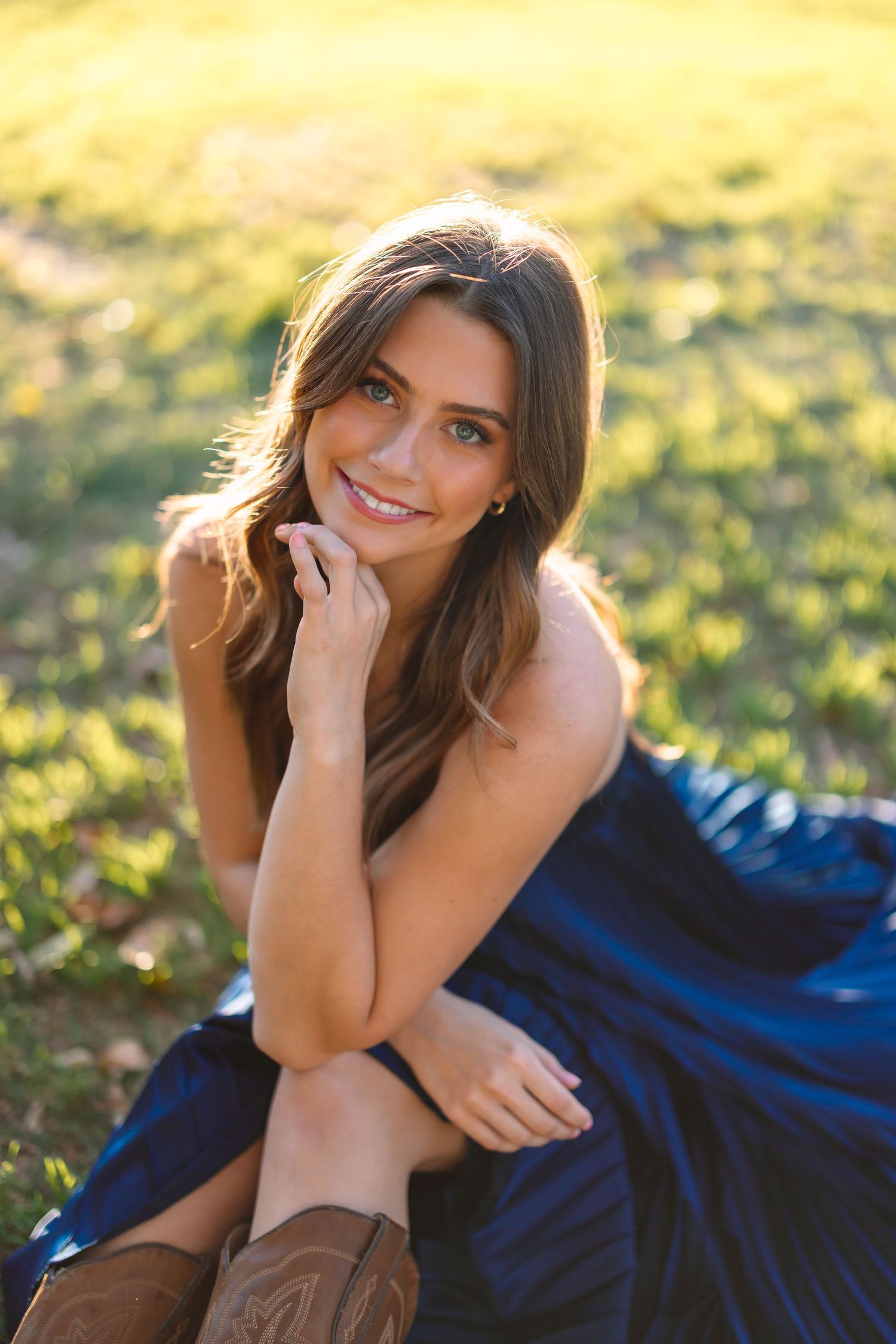 Person in navy dress poses on grass during golden hour photoshoot.