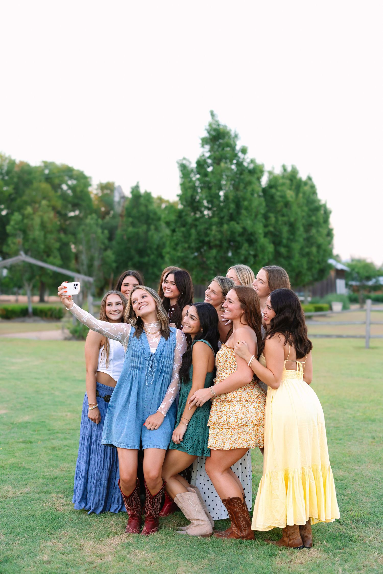 A group poses playfully on grass for photos in summer dresses and boots.