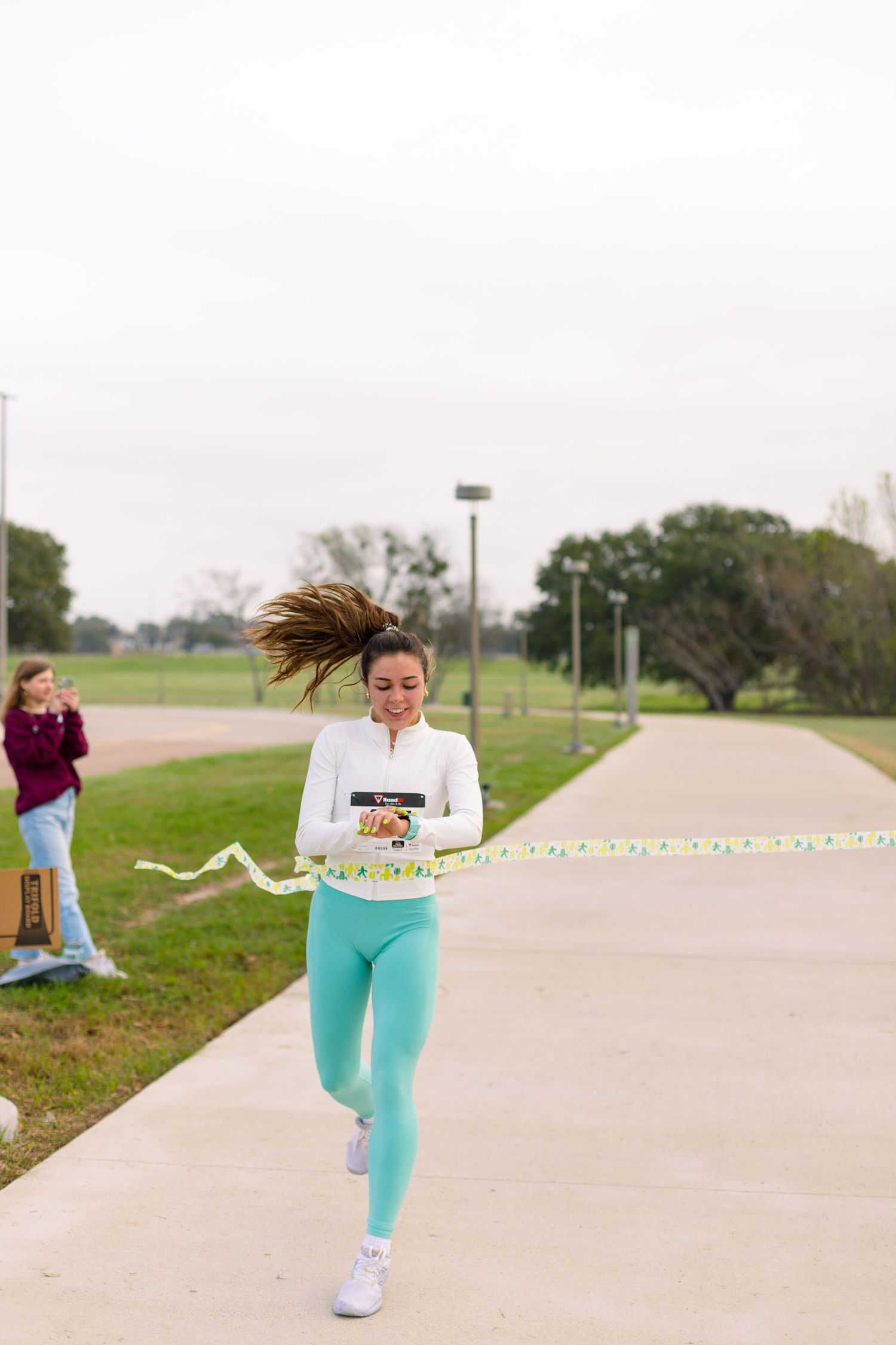 Person in turquoise pants running on a concrete path with streamers trailing behind.