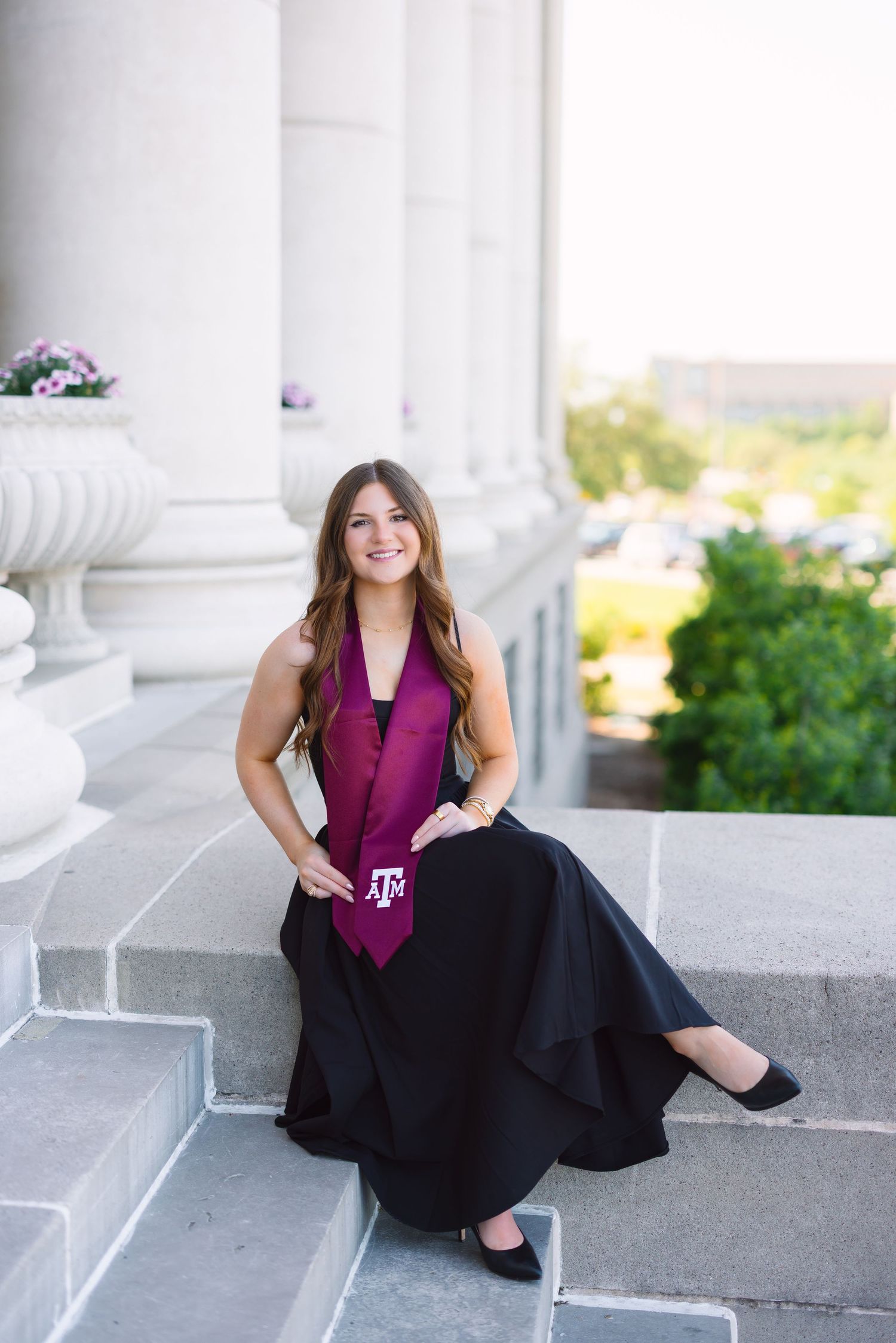 A person in graduation attire poses elegantly between white columns of a classical building.