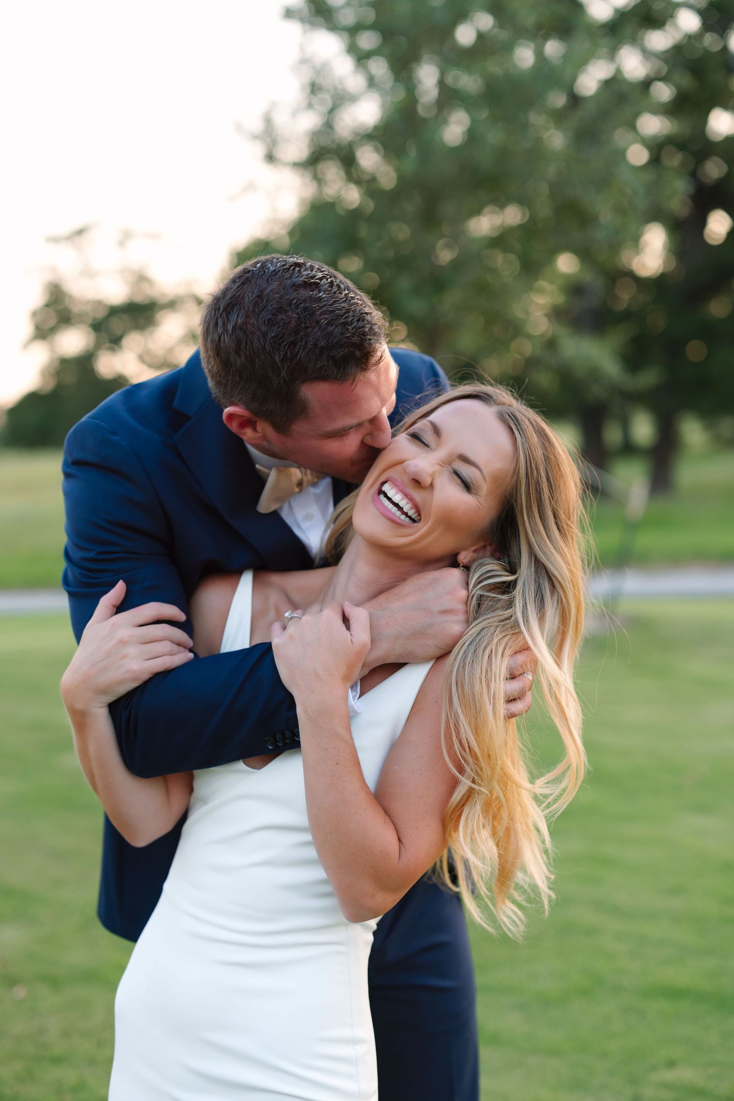 A romantic couple shares an intimate moment on grassy field during sunset.