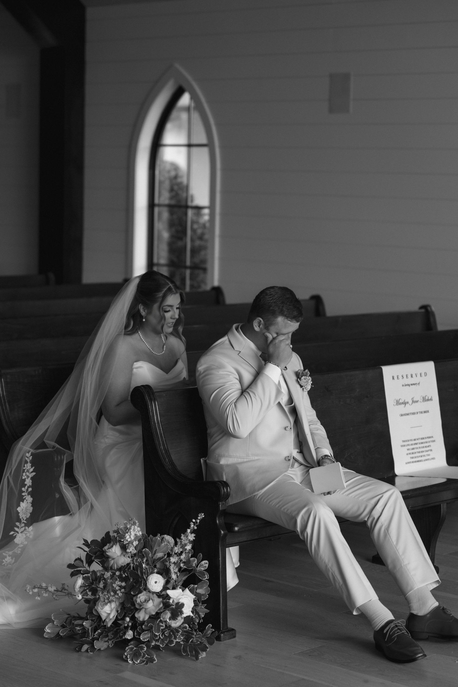 Black and white photo of bride and groom sitting separately in church pews, reading heartfelt letters before their wedding ceremony.