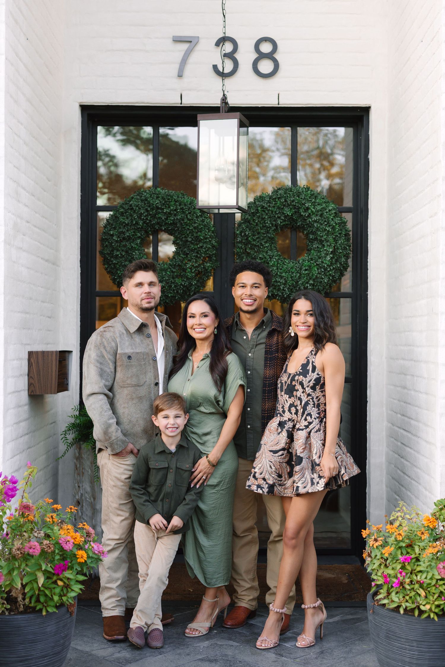 Family of five posing in front of a white brick home entrance numbered 738 with boxwood wreaths.