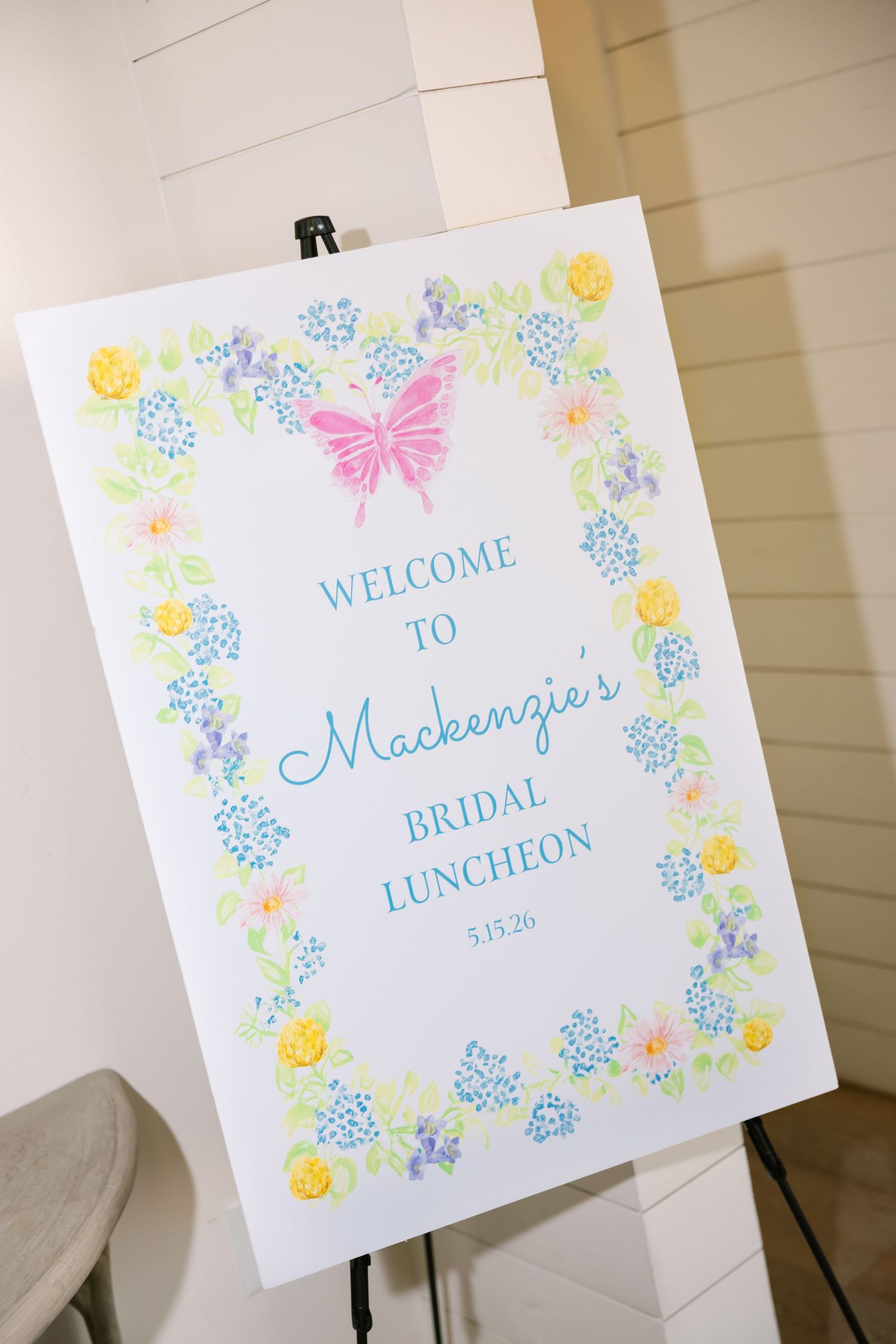 Welcome sign for Mackenzie's Bridal Luncheon on 5.15.26, decorated with colorful floral border and pink butterfly.