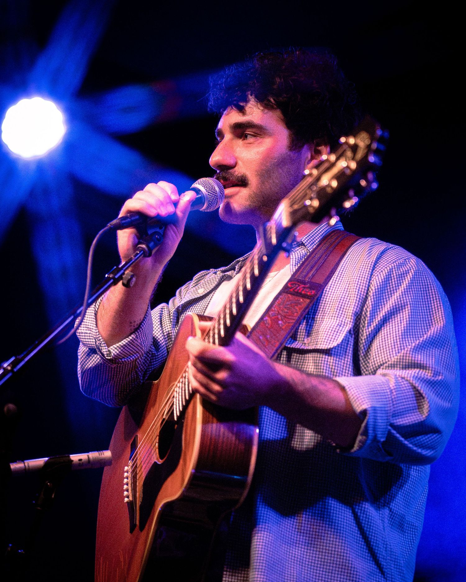 Concert performer plays acoustic guitar under dramatic blue spotlights during live show.