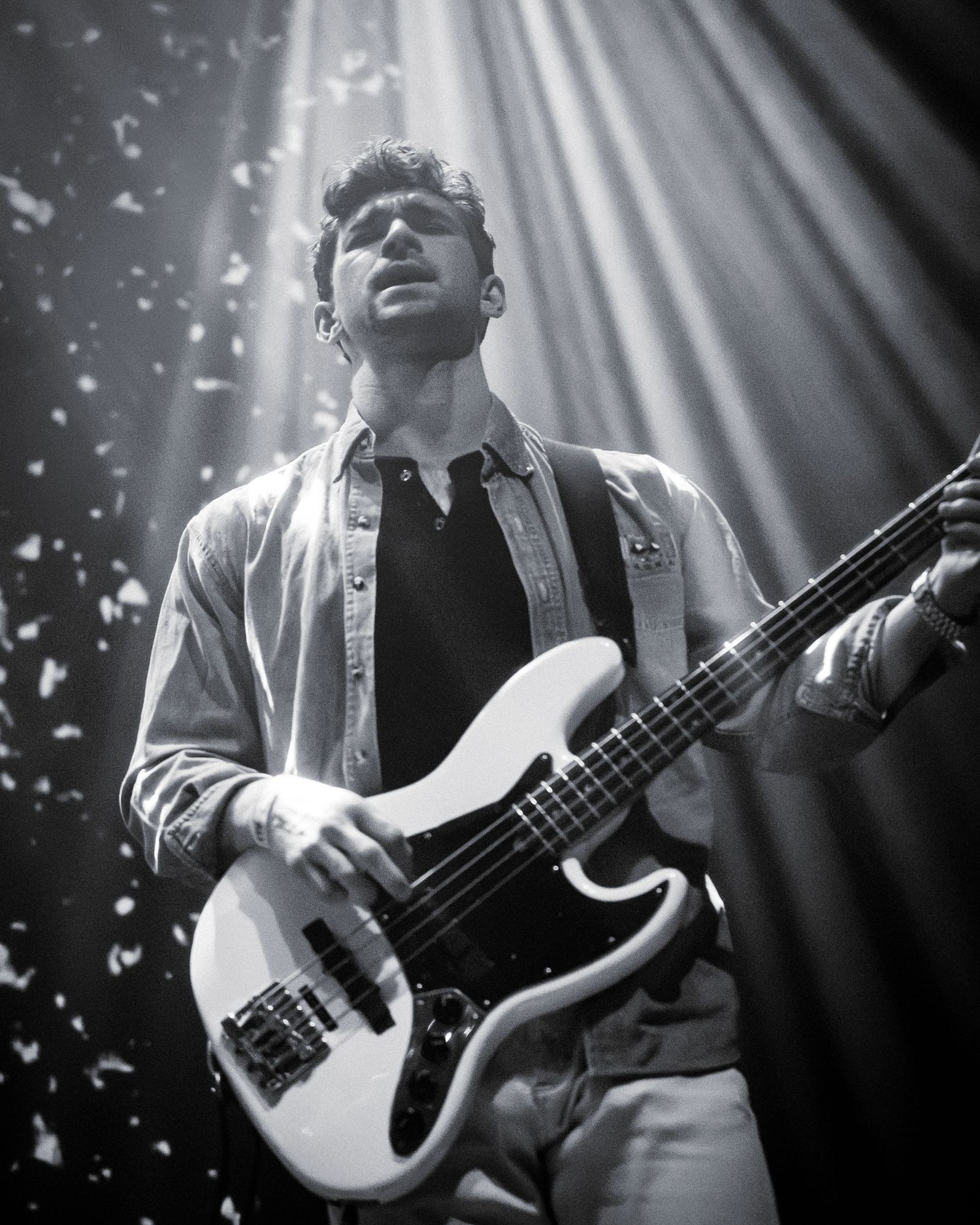 Bass guitarist performing on stage with dramatic overhead lighting and falling confetti.