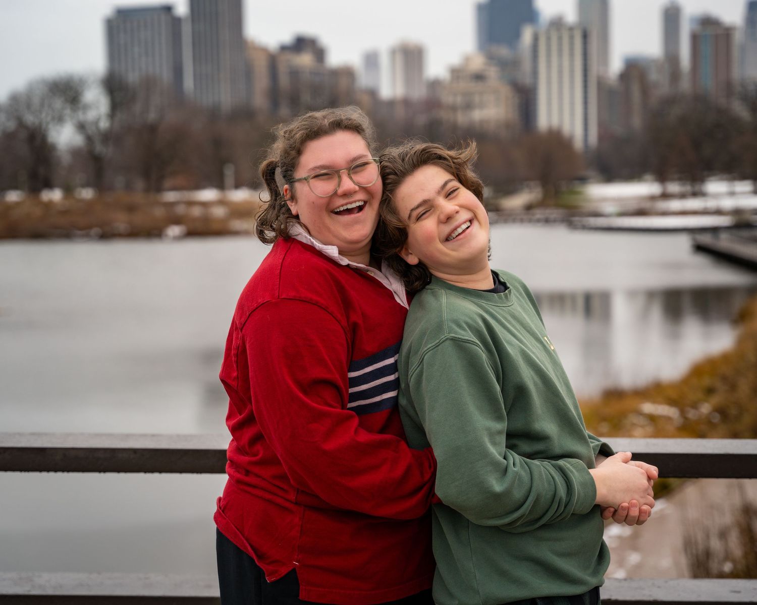 Two people embrace while smiling with the Chicago skyline and a lake visible behind them.