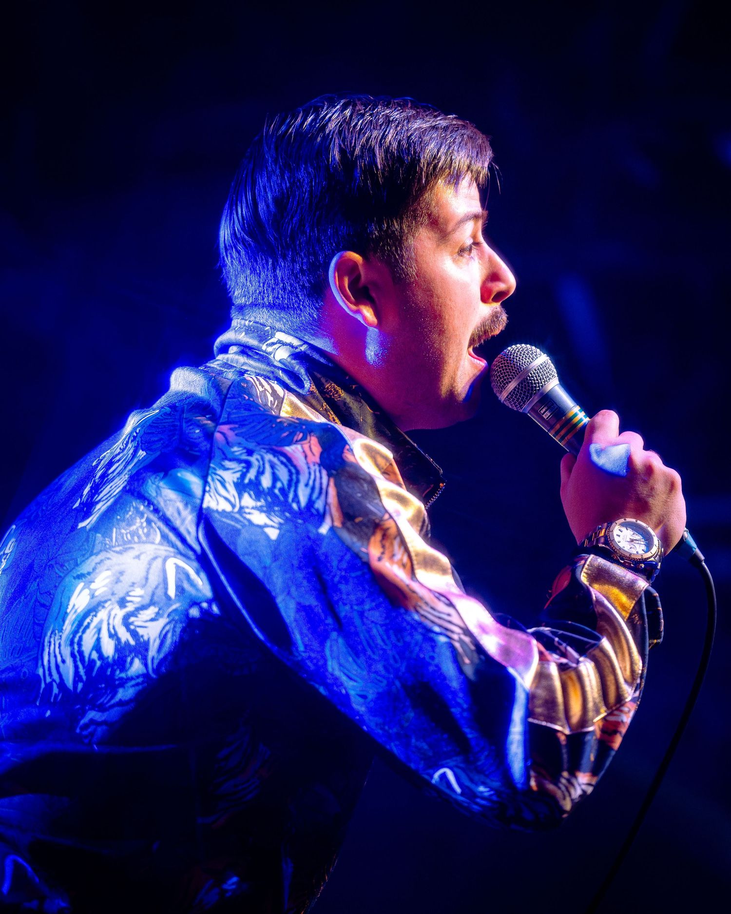 Concert performer singing passionately into microphone under dramatic blue stage lighting.