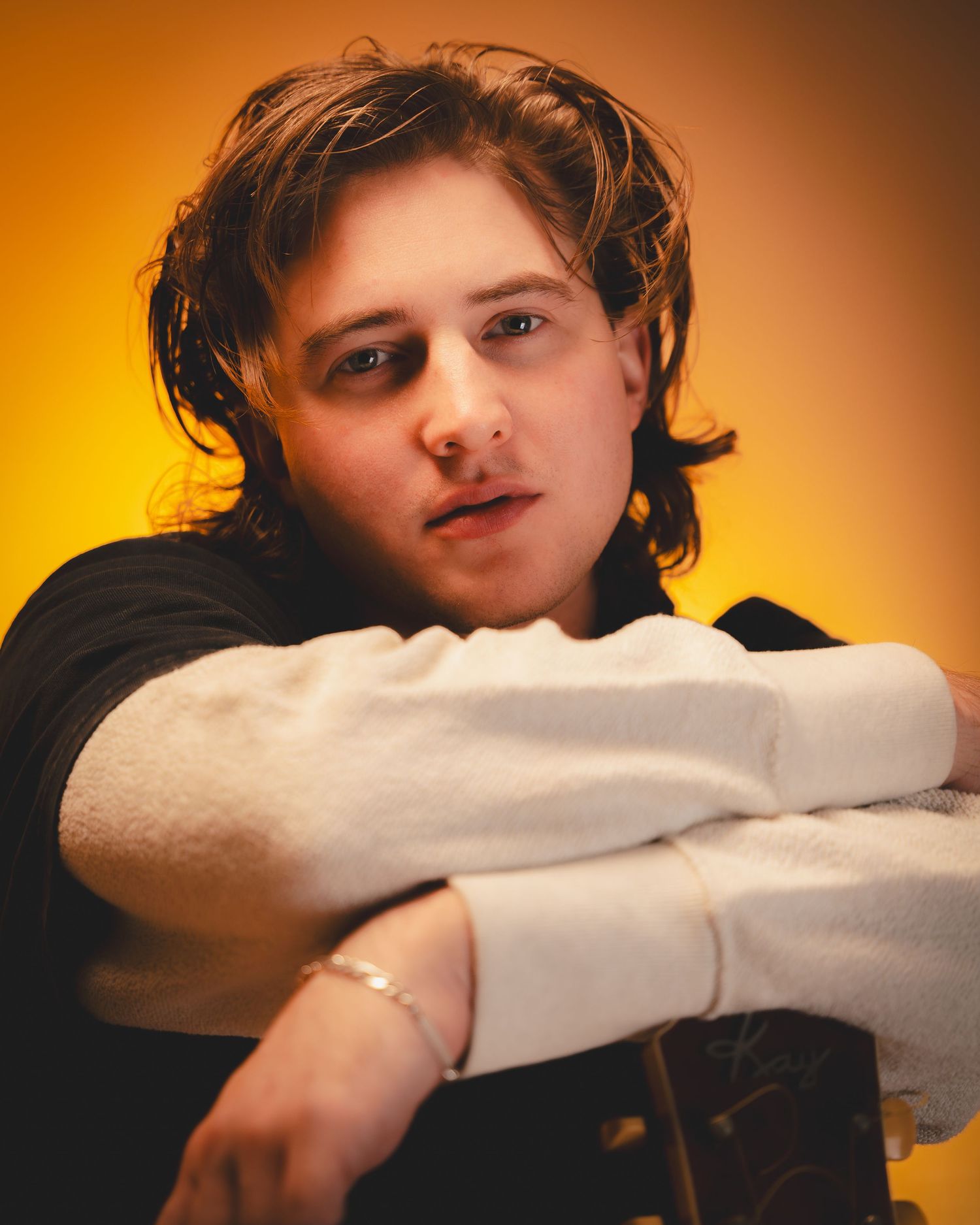 Artistic portrait of a musician in casual attire against an orange gradient background.