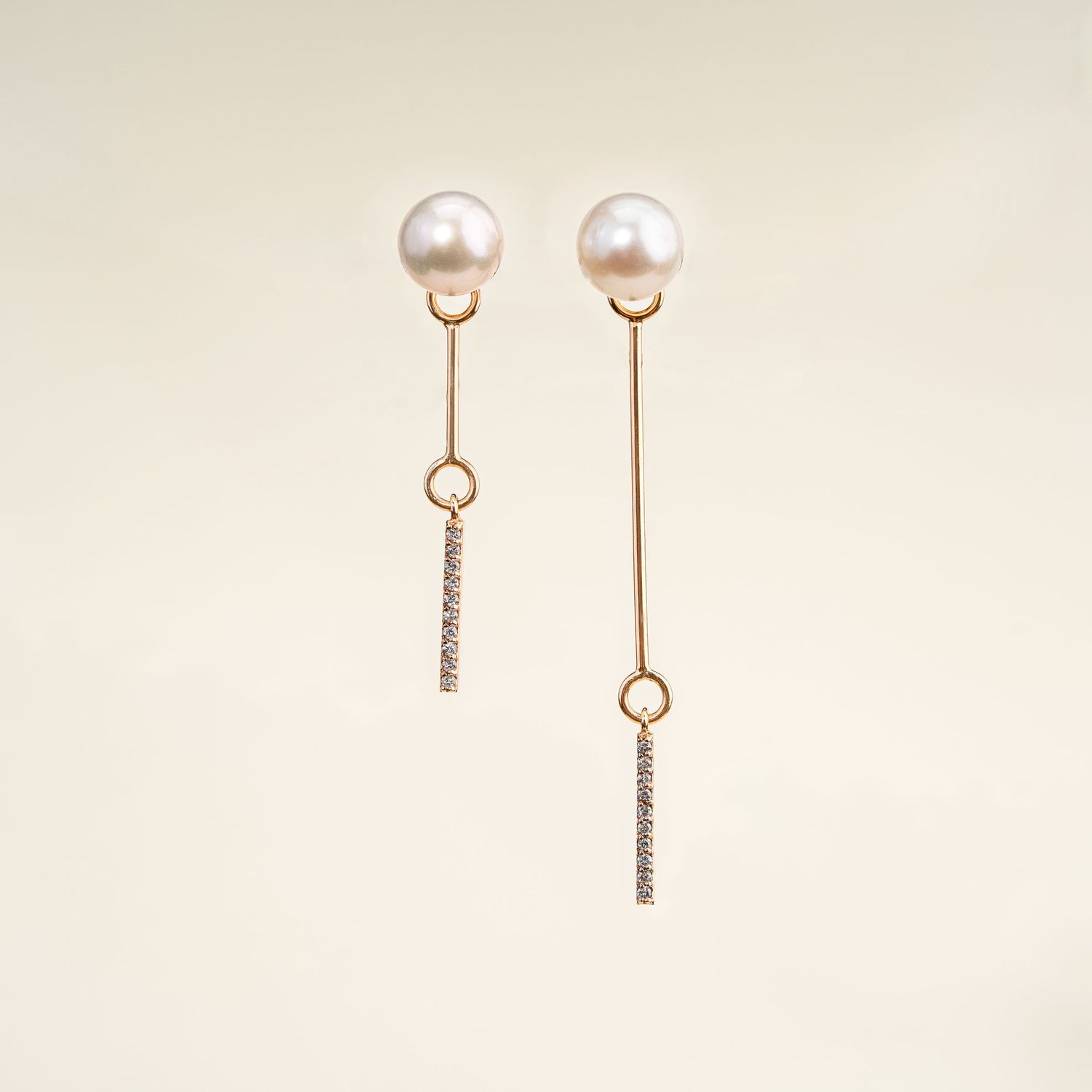 Modern pearl and crystal drop earrings in rose gold finish against white backdrop.