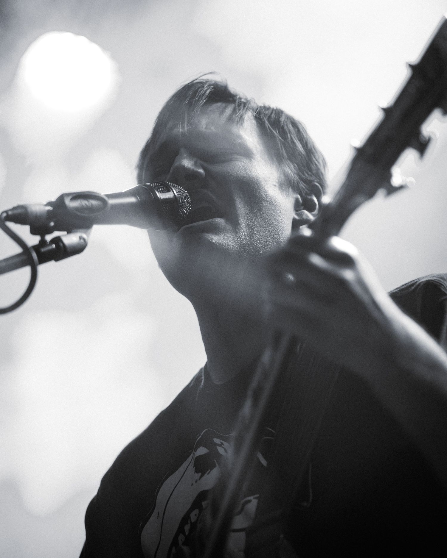 Black and white concert photo of performer singing into microphone with bright spotlight.