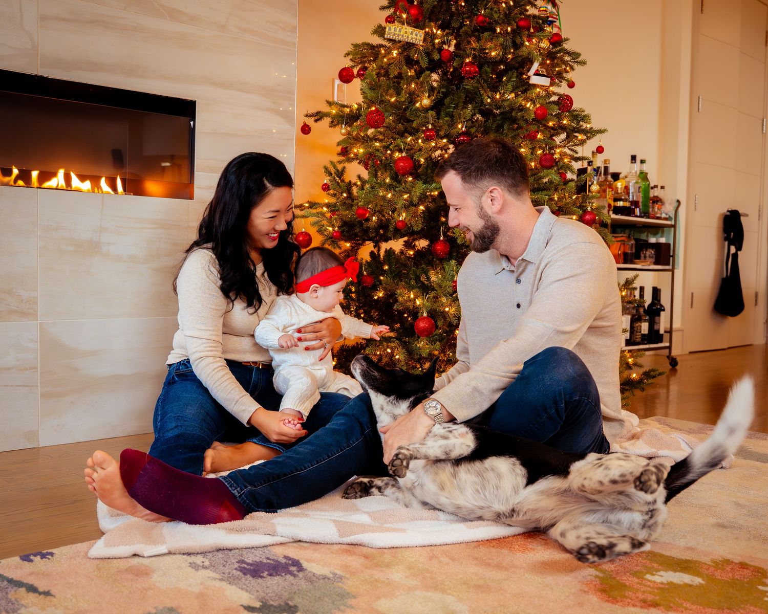A family shares a tender moment together while relaxing on a cozy blanket near a decorated Christmas tree.