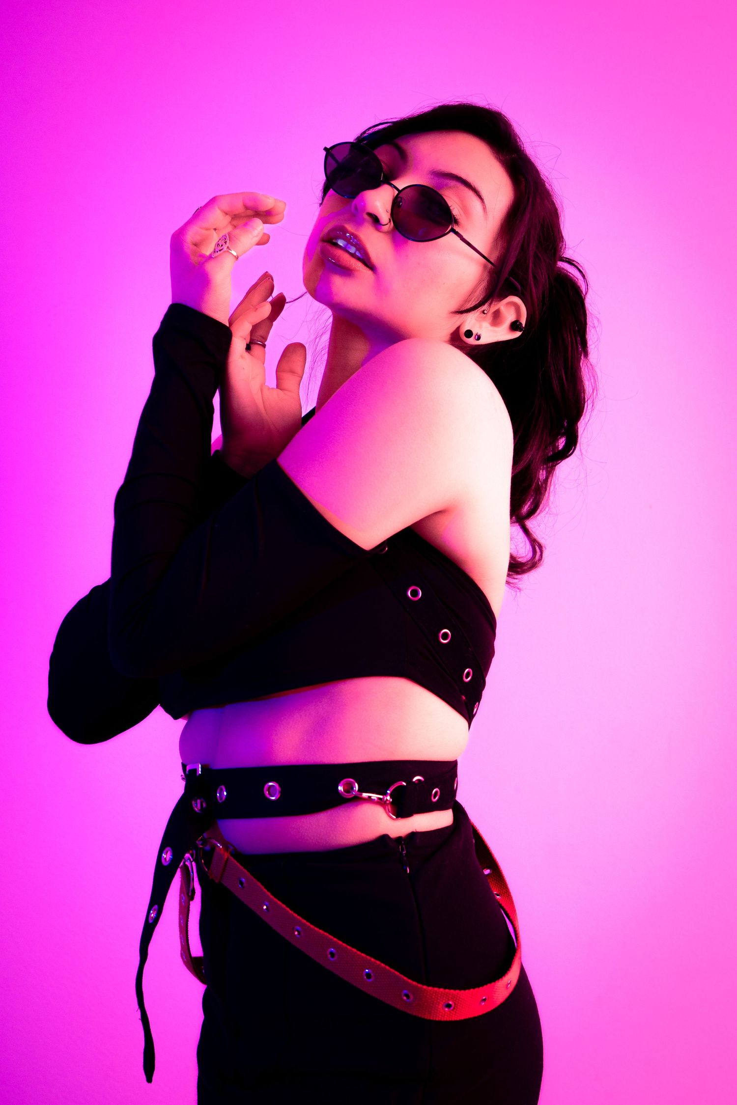 Fashion model in black crop top and belt poses dramatically against neon pink backdrop.