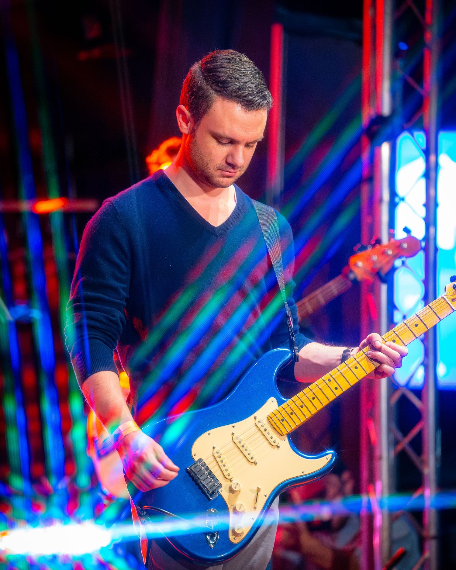 Guitarist playing electric guitar with colorful stage lighting effects.