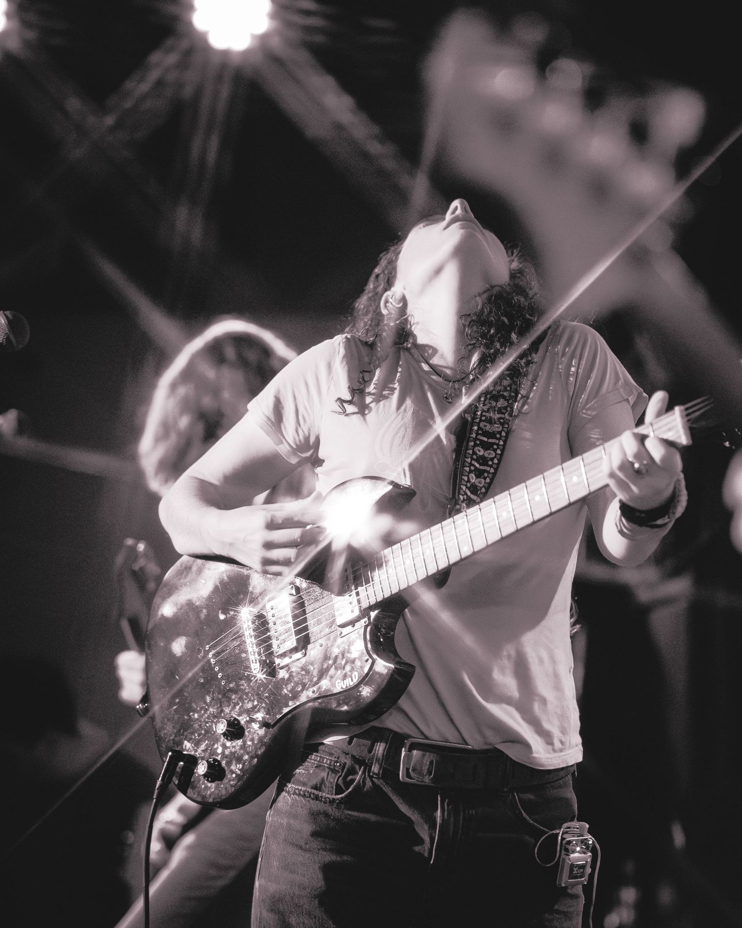 Black and white photo of a musician performing with an electric guitar on stage during a live concert.