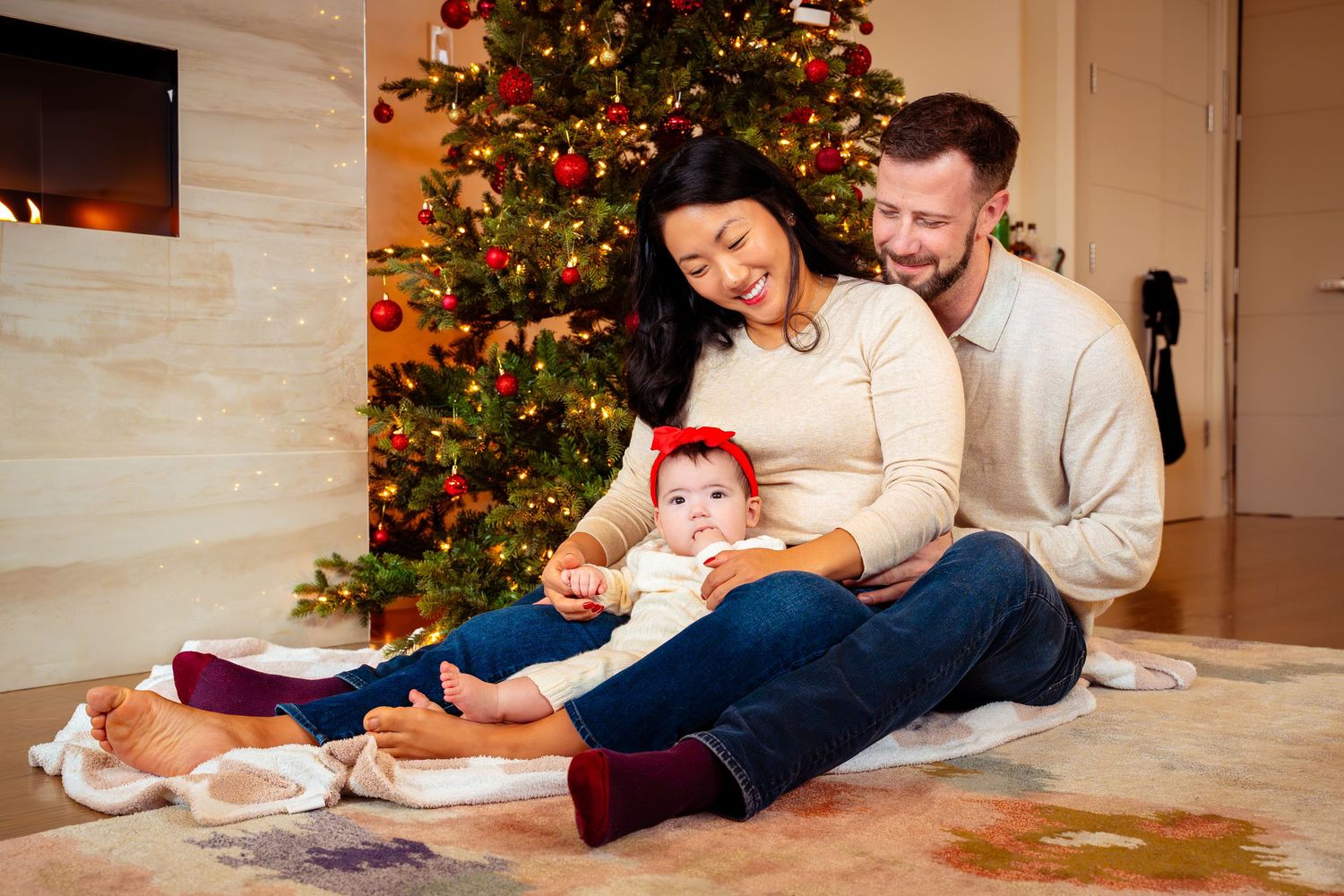 A family sits together on the floor in front of a decorated Christmas tree in their cozy living room.