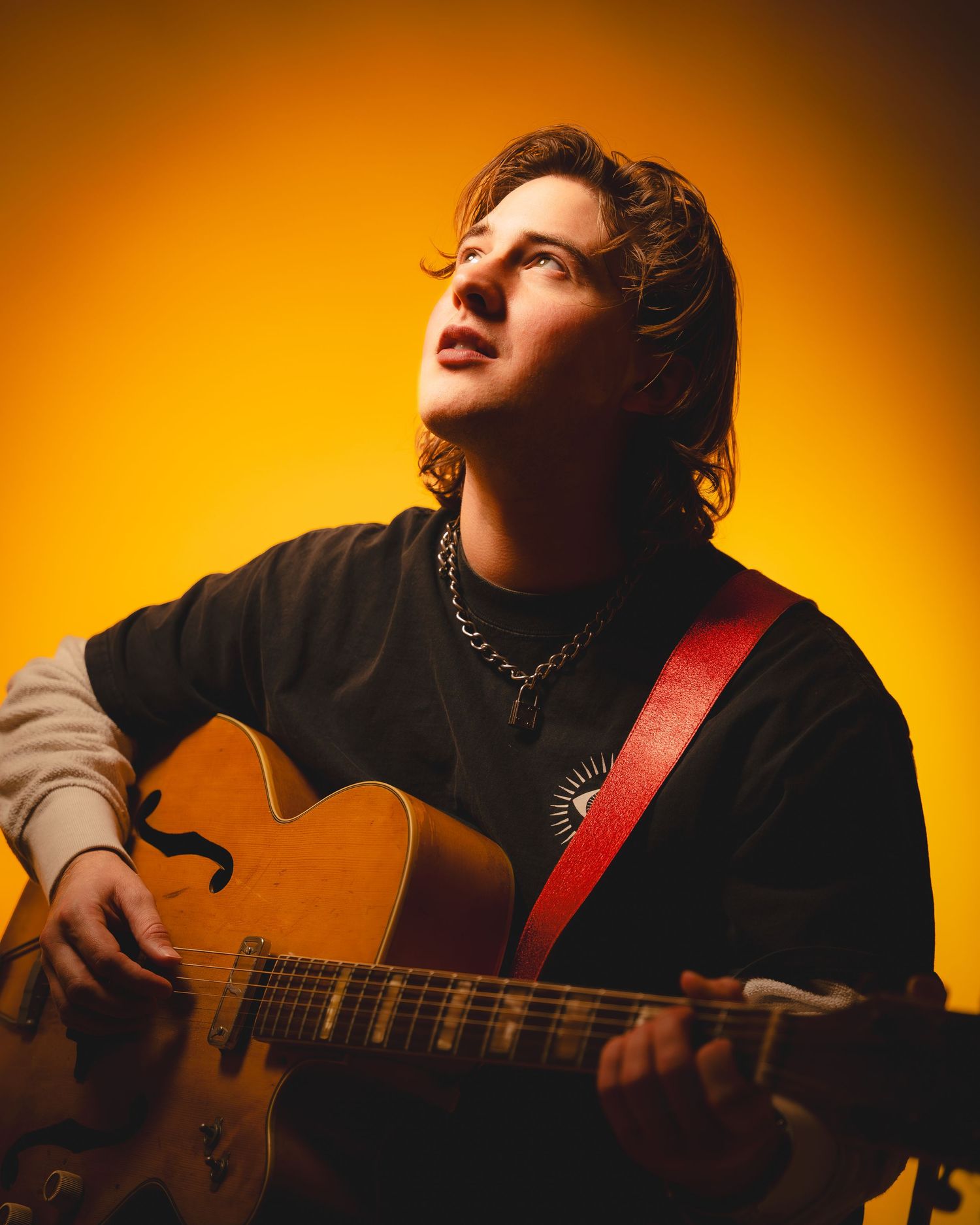 Musician plays acoustic guitar in dramatic lighting against warm orange background.