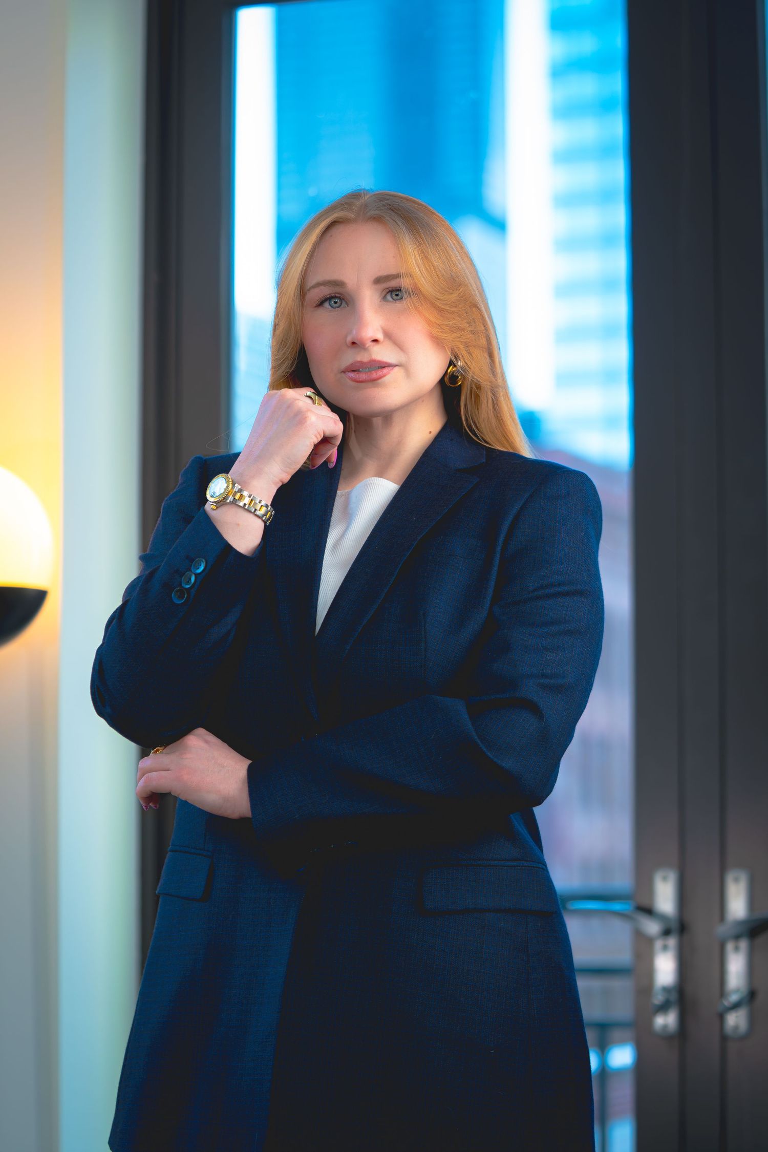 Professional woman in navy blazer poses confidently against modern office backdrop with blue lighting.