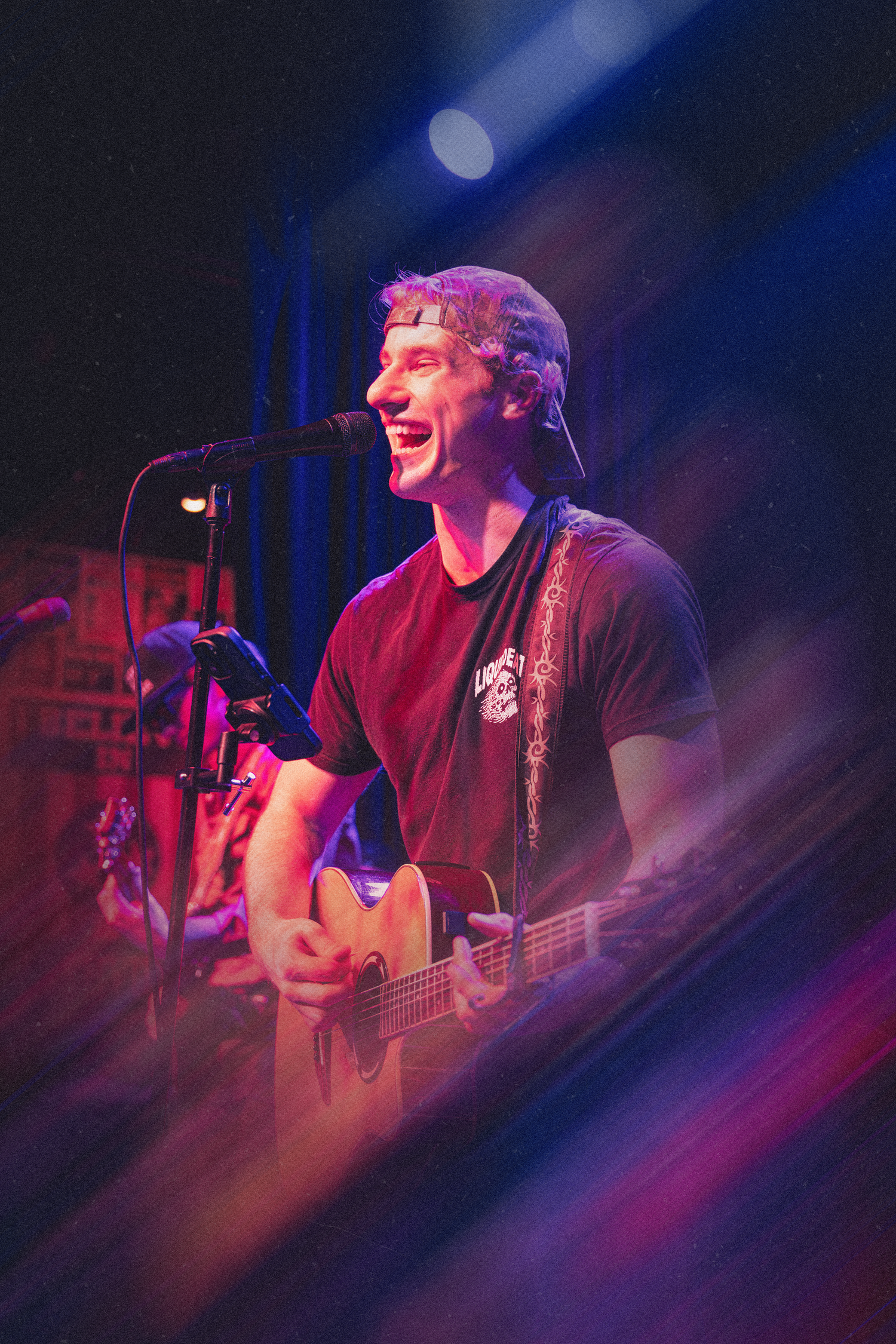 Musician performing on stage bathed in purple and red lighting during a live concert performance.