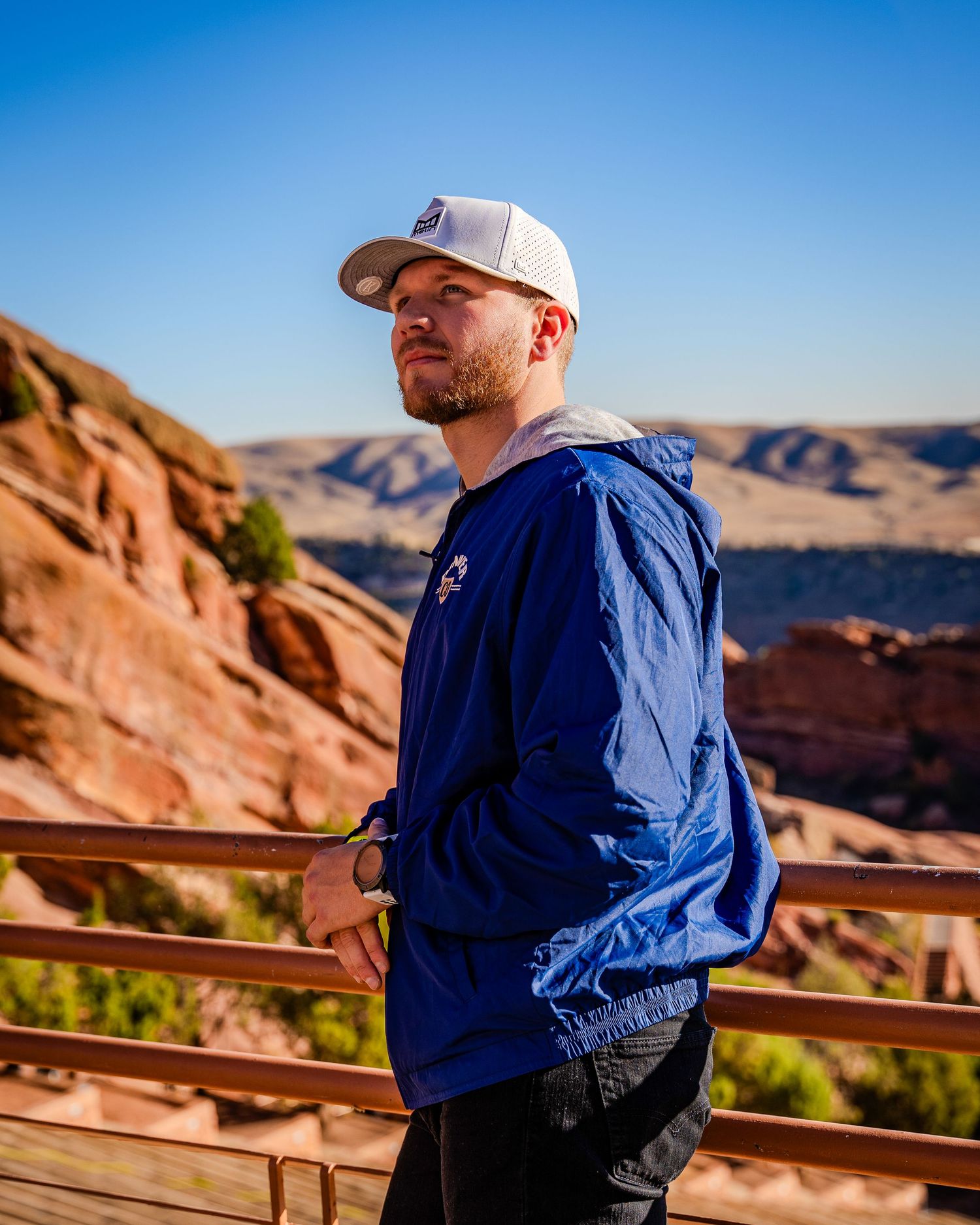Hiker in blue windbreaker and cap overlooking scenic desert canyon vista.